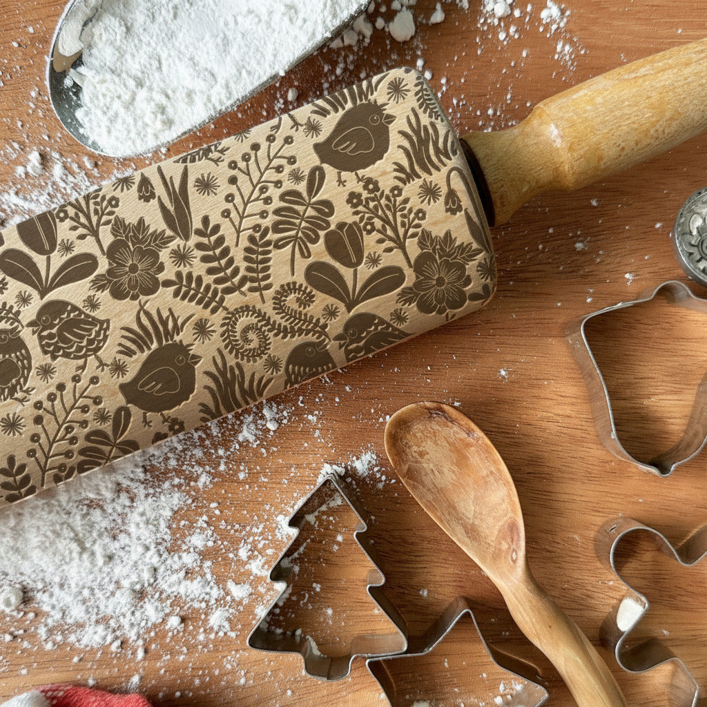 Decorative rolling pin with floral pattern and cookie cutters on a wooden surface.