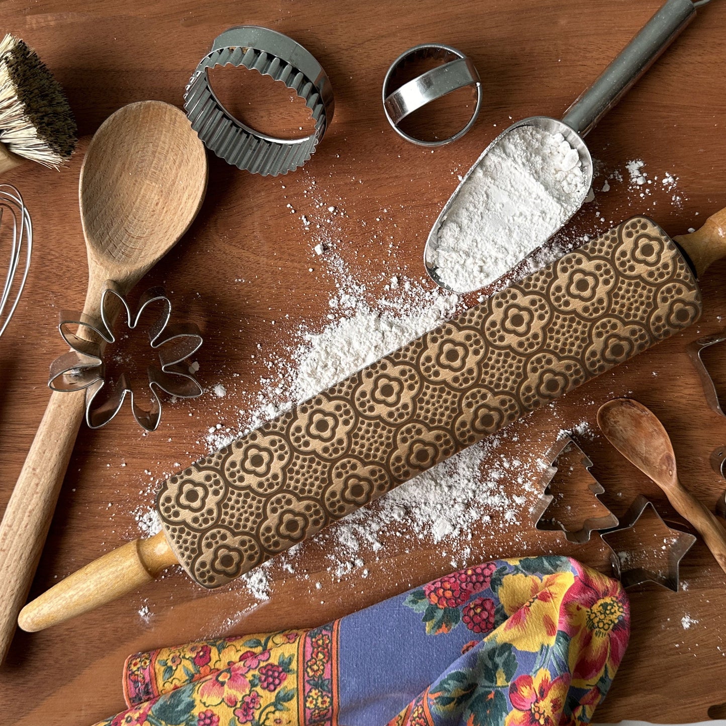 Wooden rolling pin with decorative patterns on a wooden surface with flour and kitchen tools.