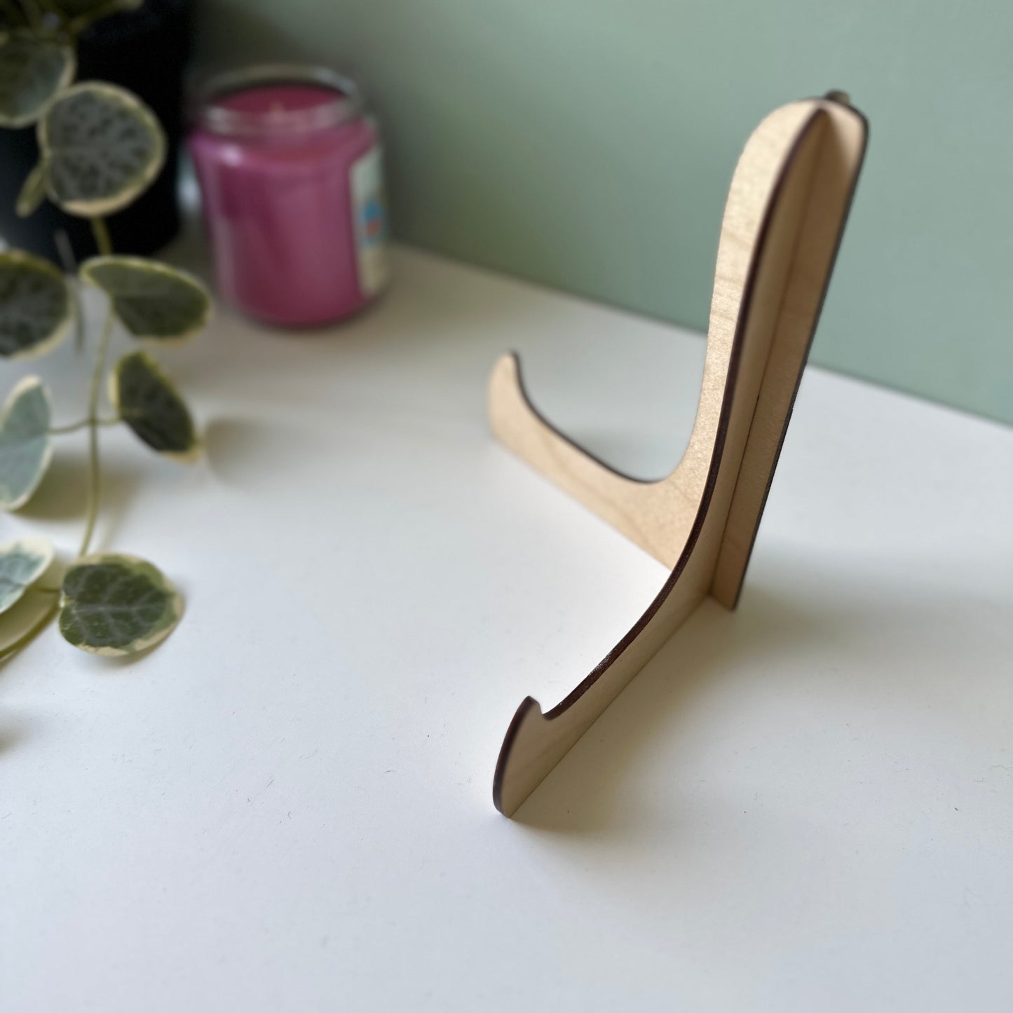 Wooden stand on a white surface with a plant and candle in the background