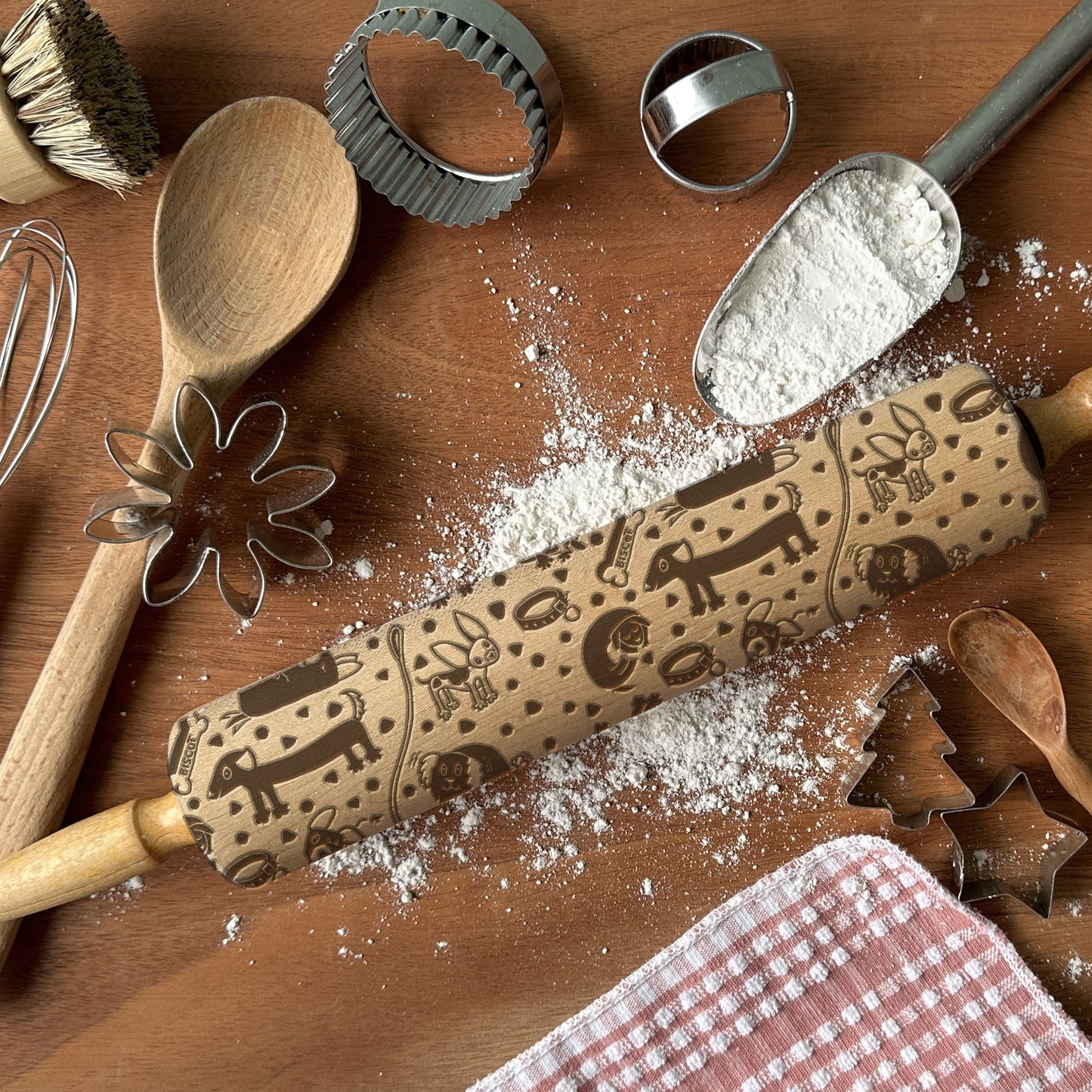 Baking tools including a rolling pin with embossed designs on a wooden surface with flour.