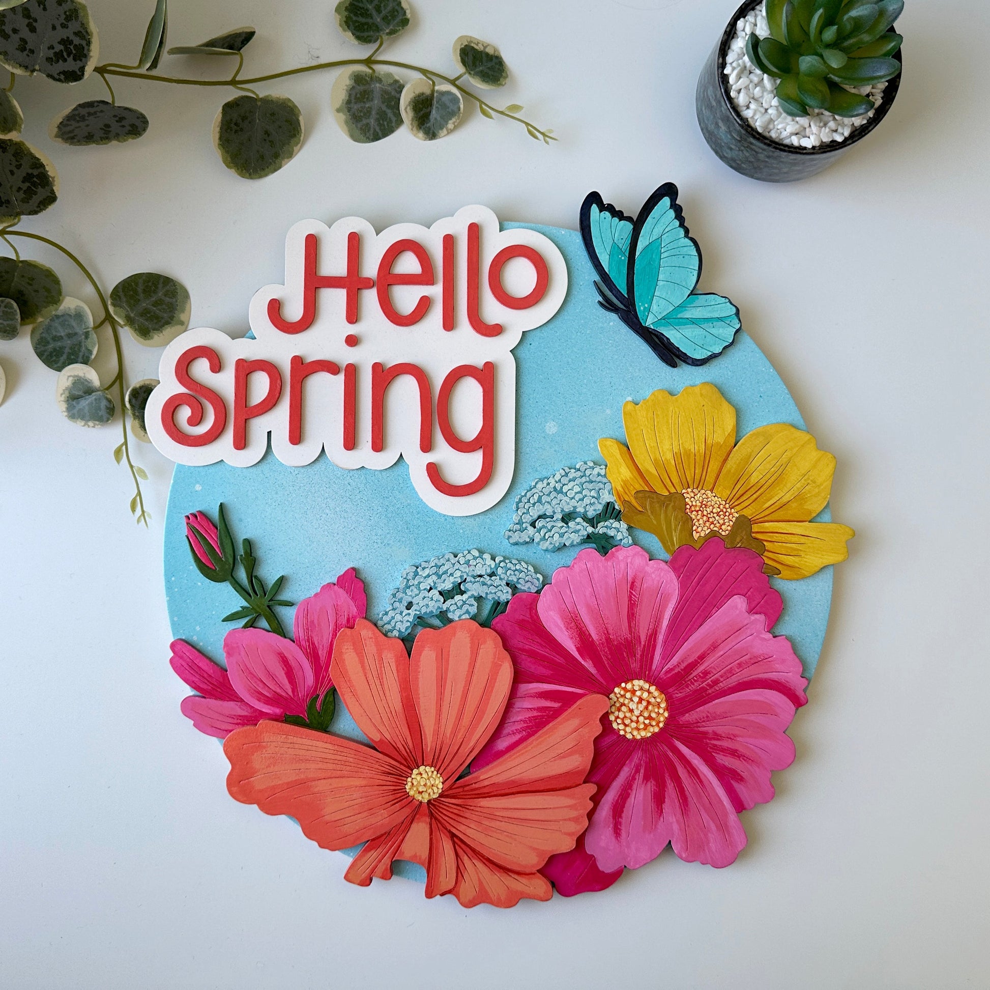 Decorative sign with 'Hello Spring' text, colorful flowers, and a butterfly on a light background.