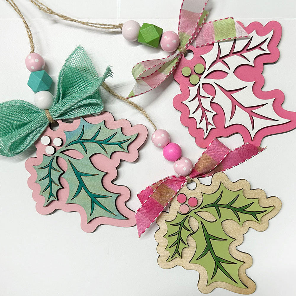 Decorative Christmas holly leaf ornaments with pink and green ribbons on a white background