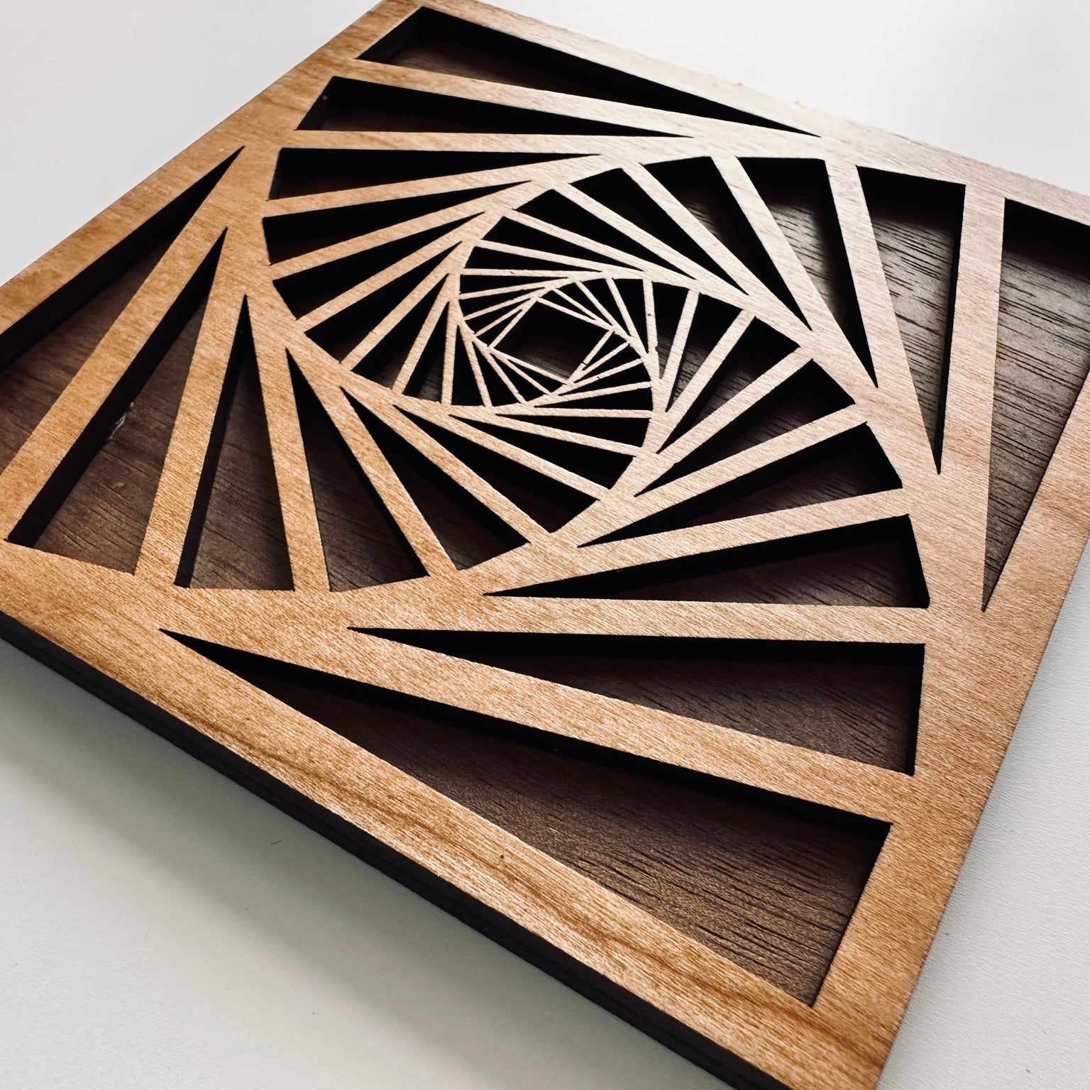 Wooden geometric coaster with a spiral design on a white background