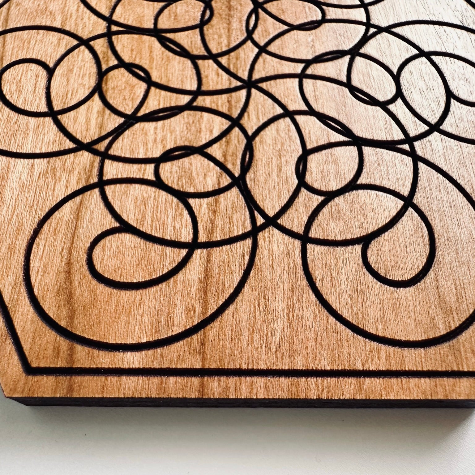 Wooden coaster with black interlocking shapes on a light background