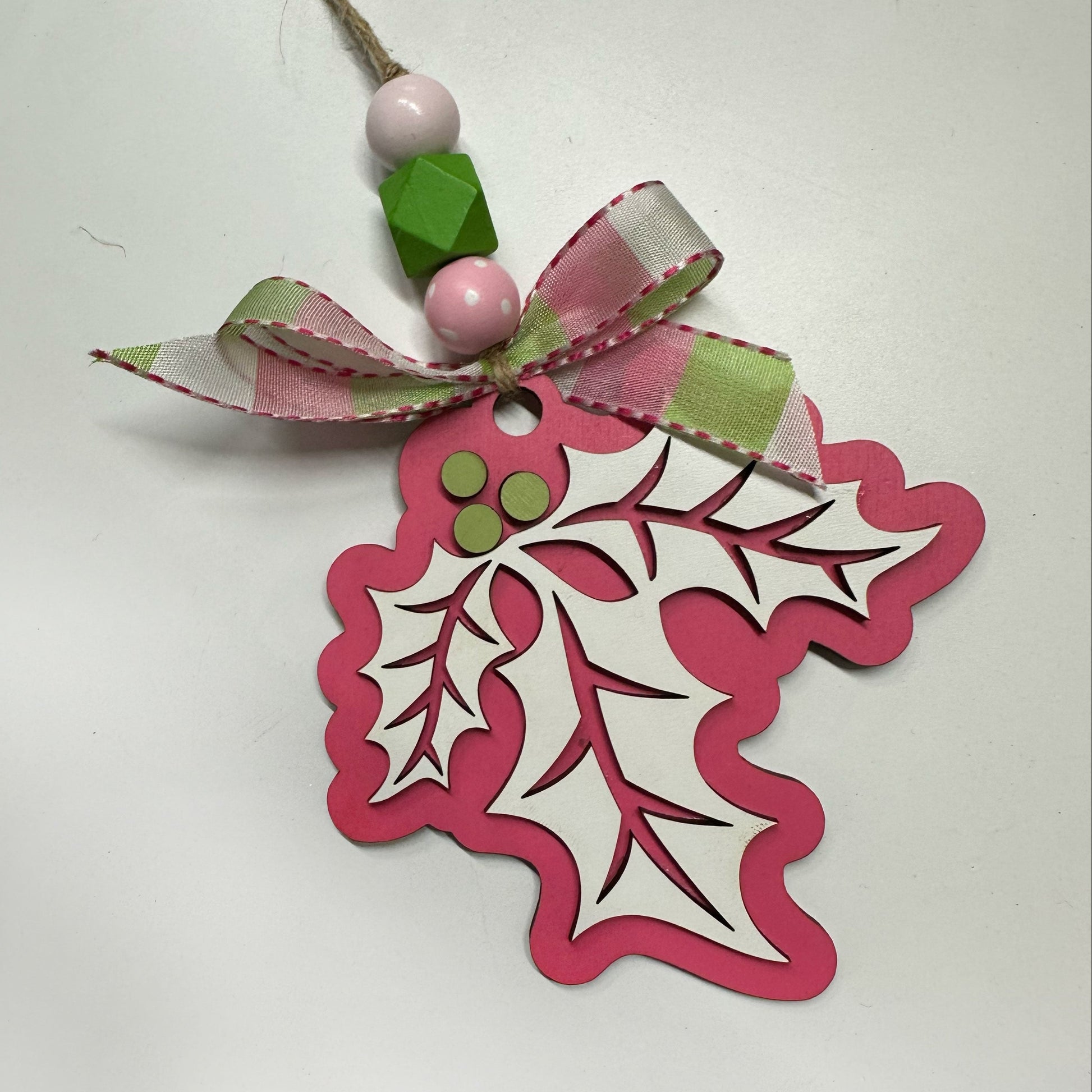 Decorative holly leaf ornament with pink border and ribbon on a white background