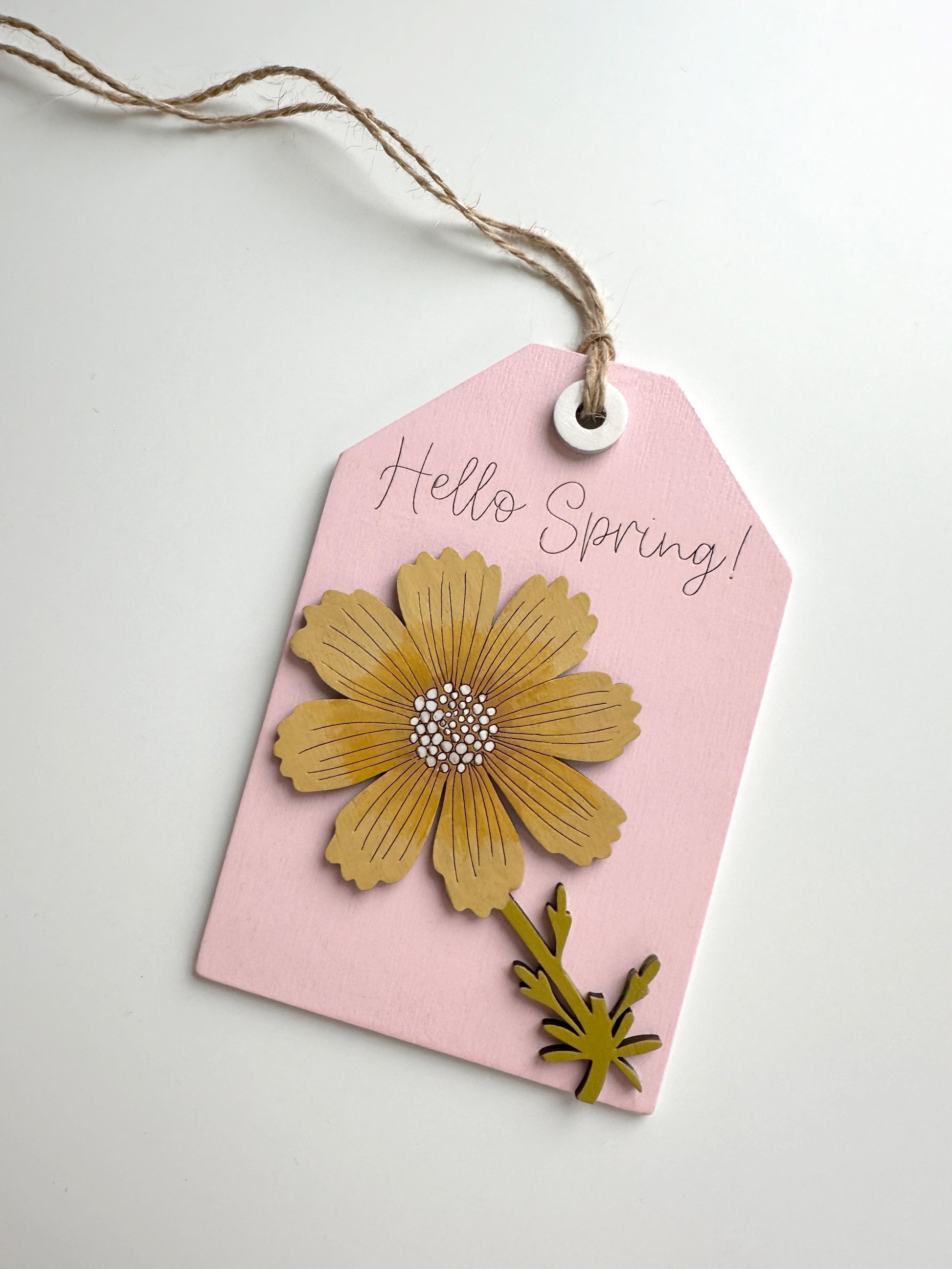 Pink tag with a yellow flower design and 'Hello Spring!' text on a light gray background
