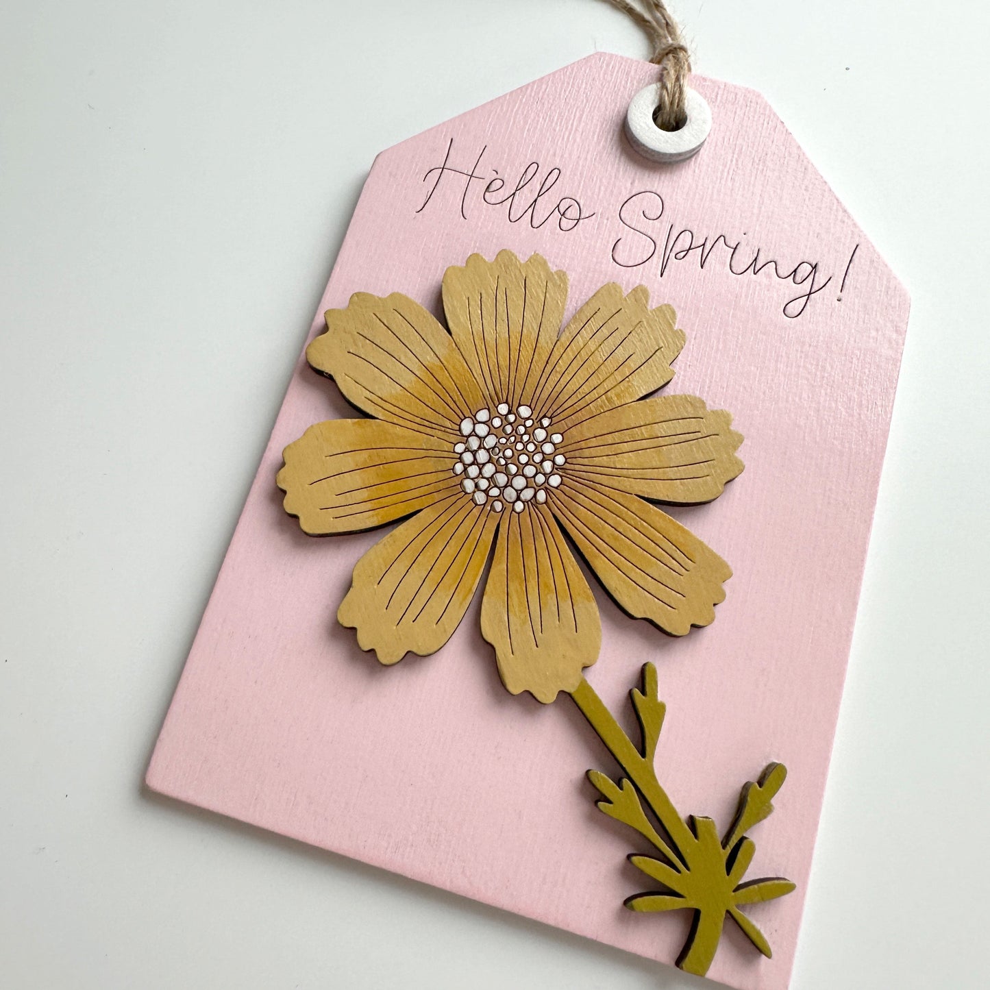 Pink tag with gold floral design and 'Hello Spring!' text on a light gray background