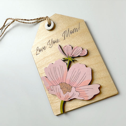 Kraft paper tag with pink floral cutout and string on a light gray background