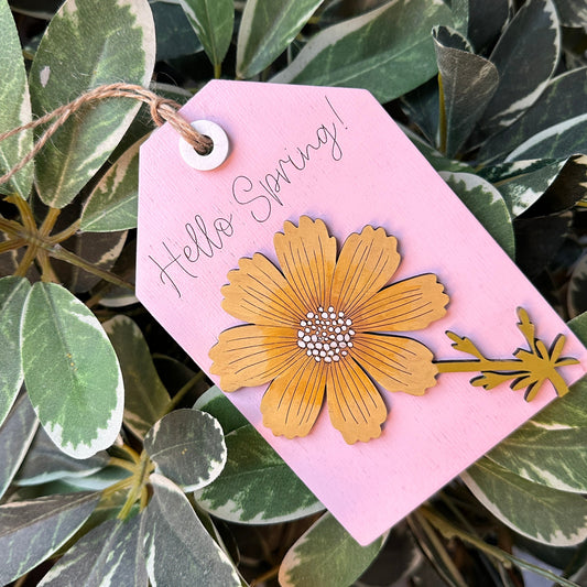 Pink tag with a yellow flower design hanging among green leaves