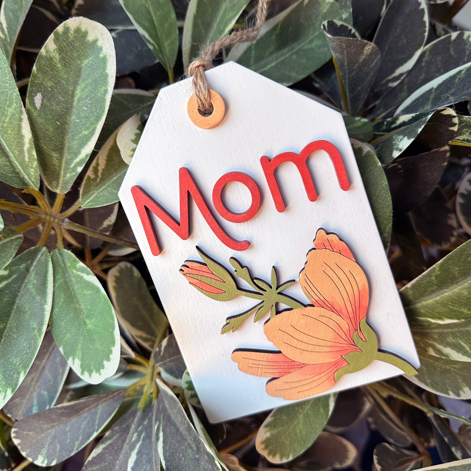 Decorative tag with 'Mom' and floral design on green leaves