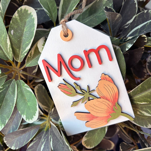 Decorative tag with 'Mom' and floral design on green leaves