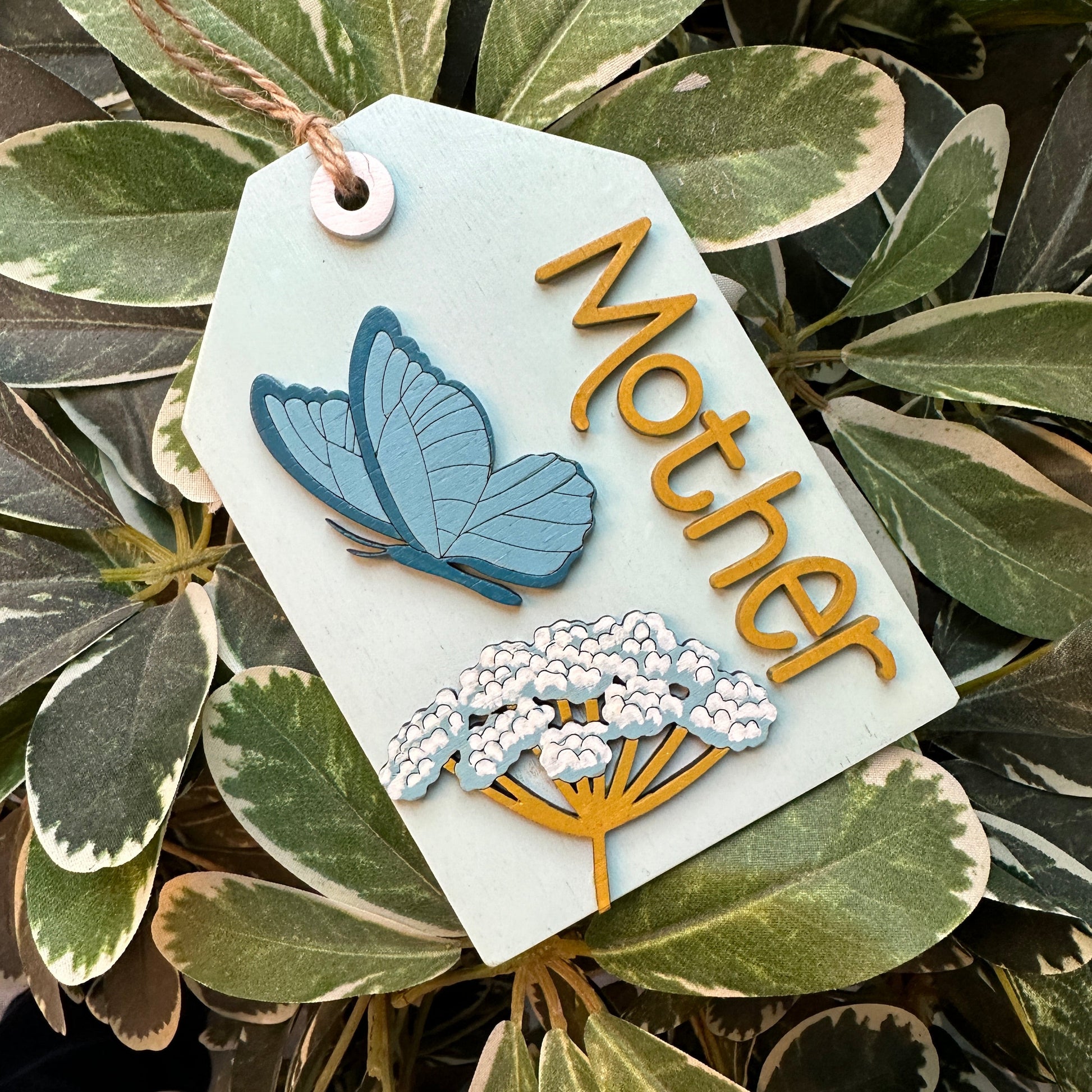 Decorative tag with 'Mother' and butterfly design on green leaves