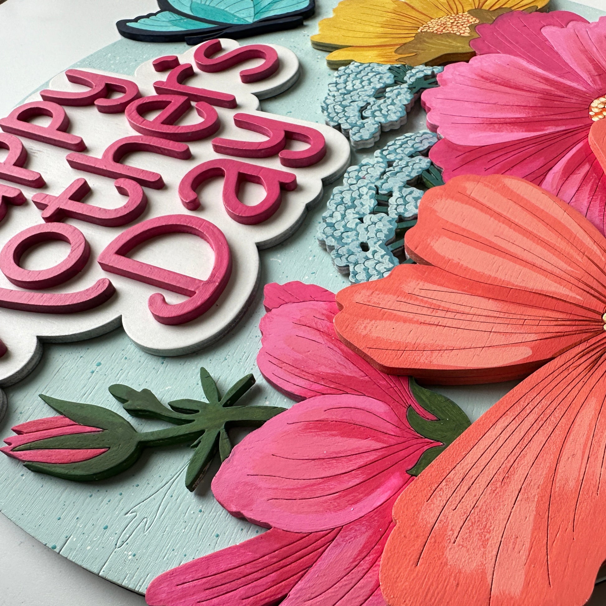 Decorative card with 'Happy Mother's Day' text and large pink flowers on a light blue background.