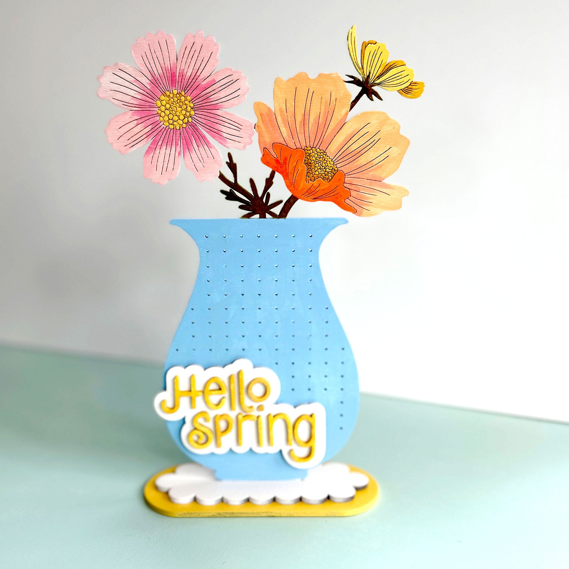 Decorative vase with flowers and 'Hello Spring' text on a light background