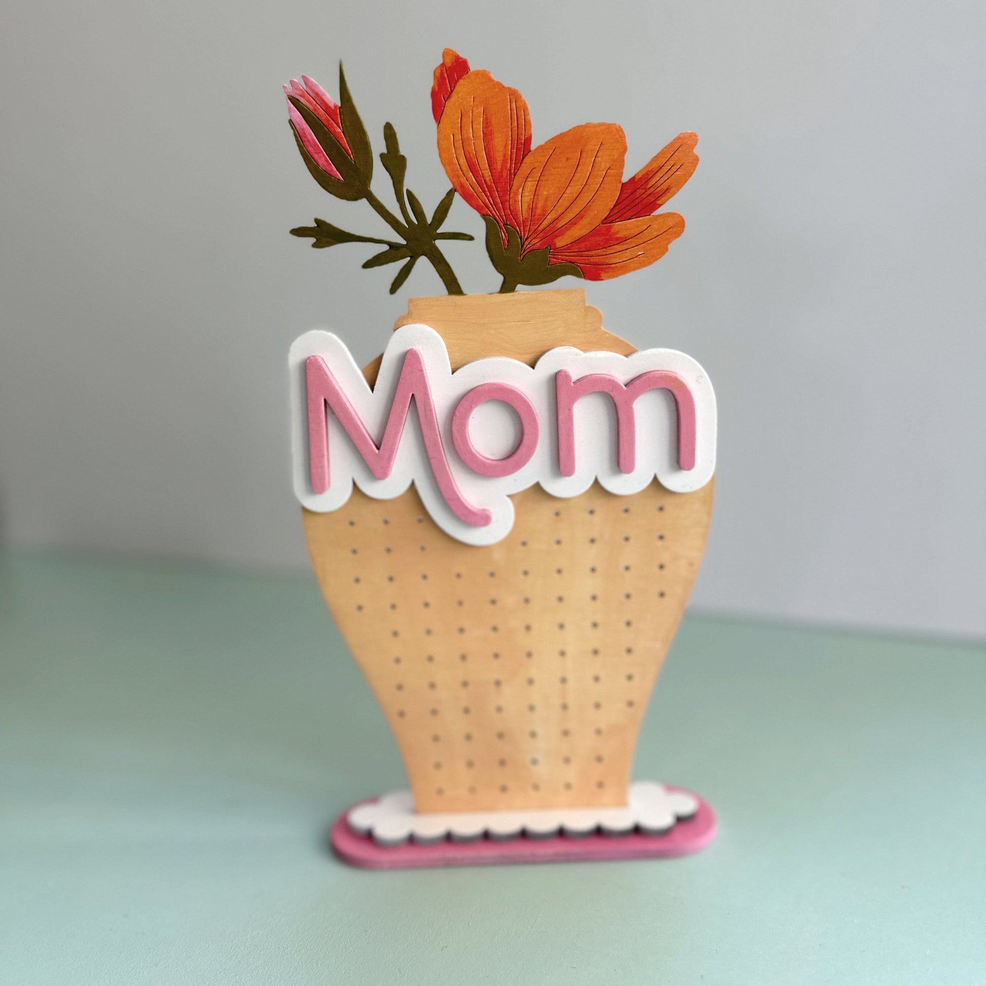 Decorative earring stand with flowers and 'Mom' text on a light blue background
