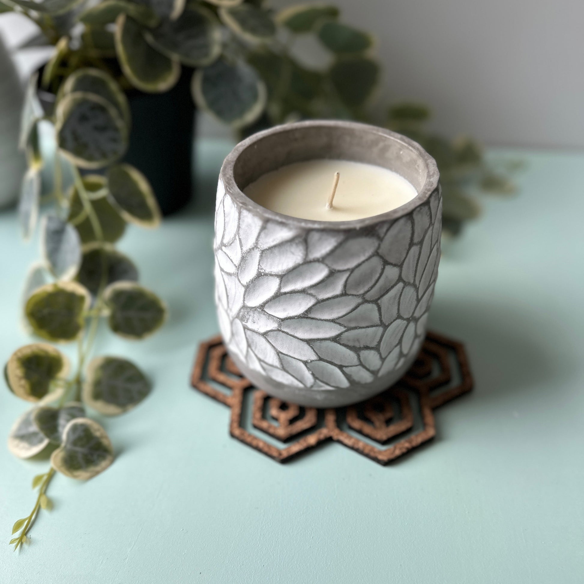 White candle in a glass jar on a honeycomb trivet on a light background