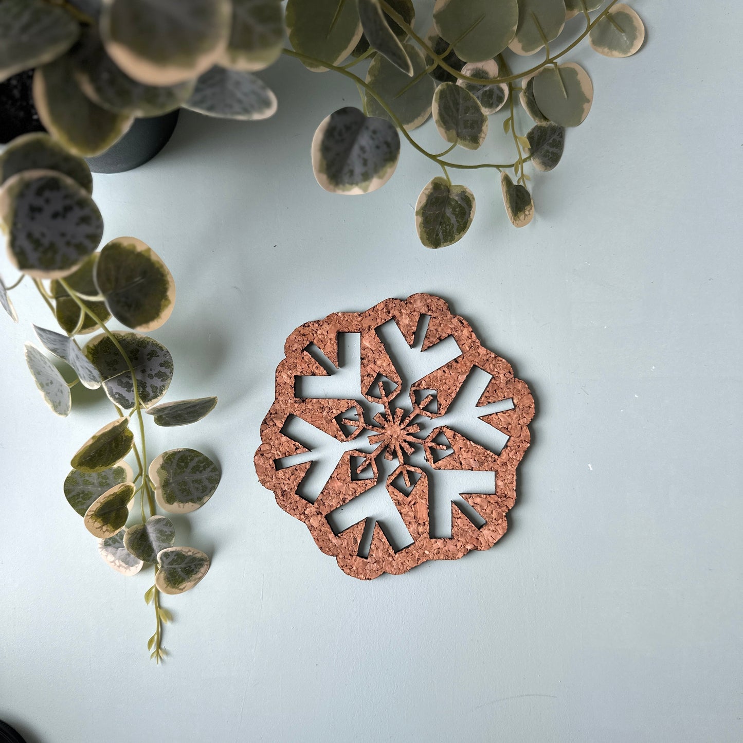 Decorative cork snowflake trivet on a white surface with green leaves in the background