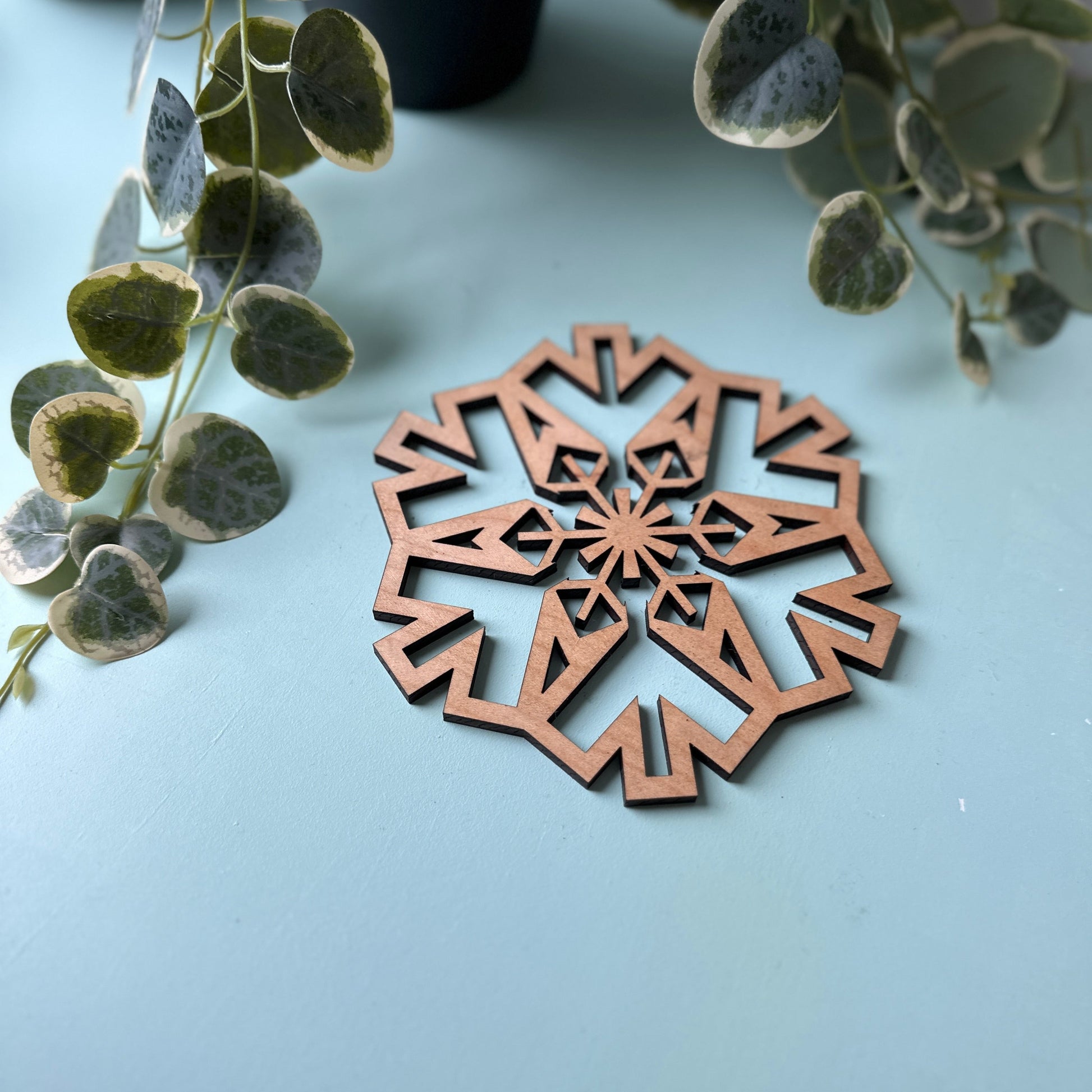 Decorative cork snowflake trivet on a light blue surface with green leaves in the background