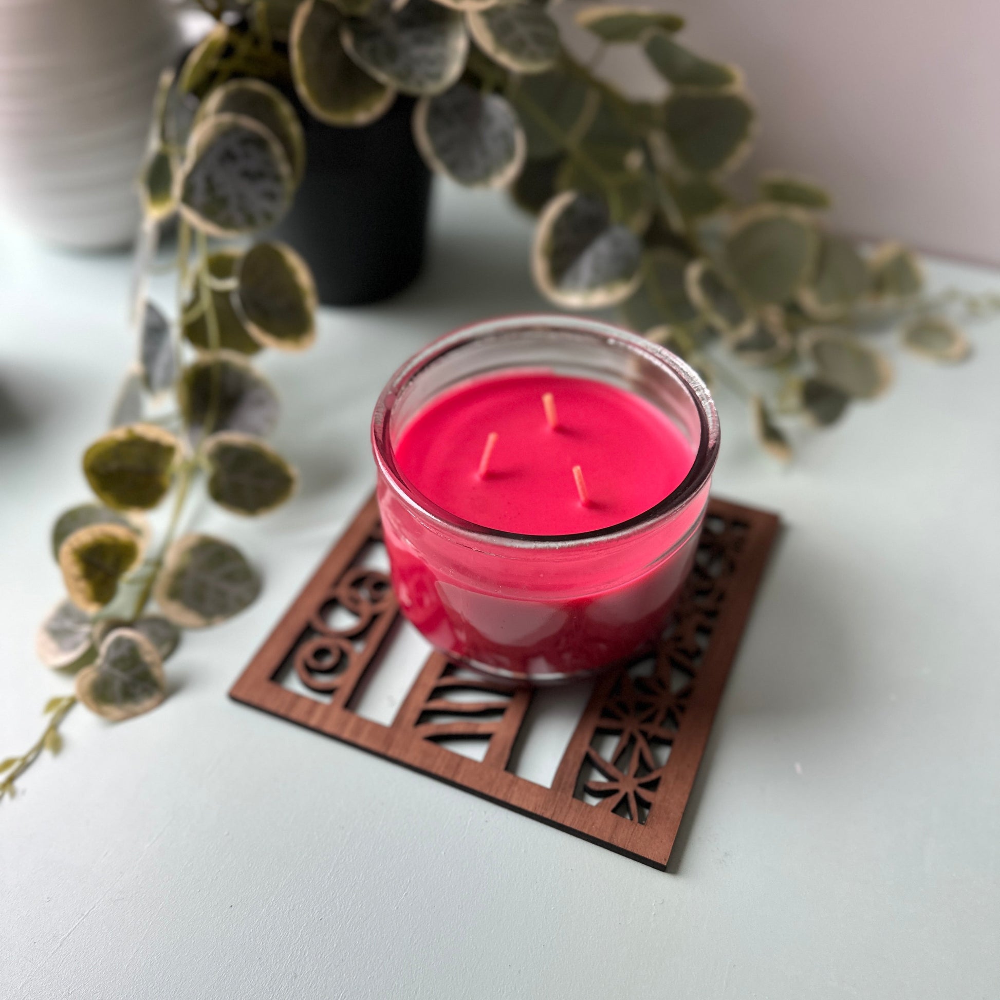 Pink candle in a glass holder on a decorative trivet with green leaves in the background
