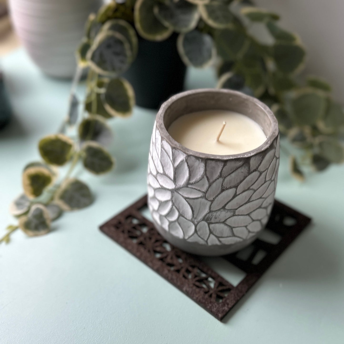 Ceramic candle holder with a lit candle on a  trivet with greenery in the background