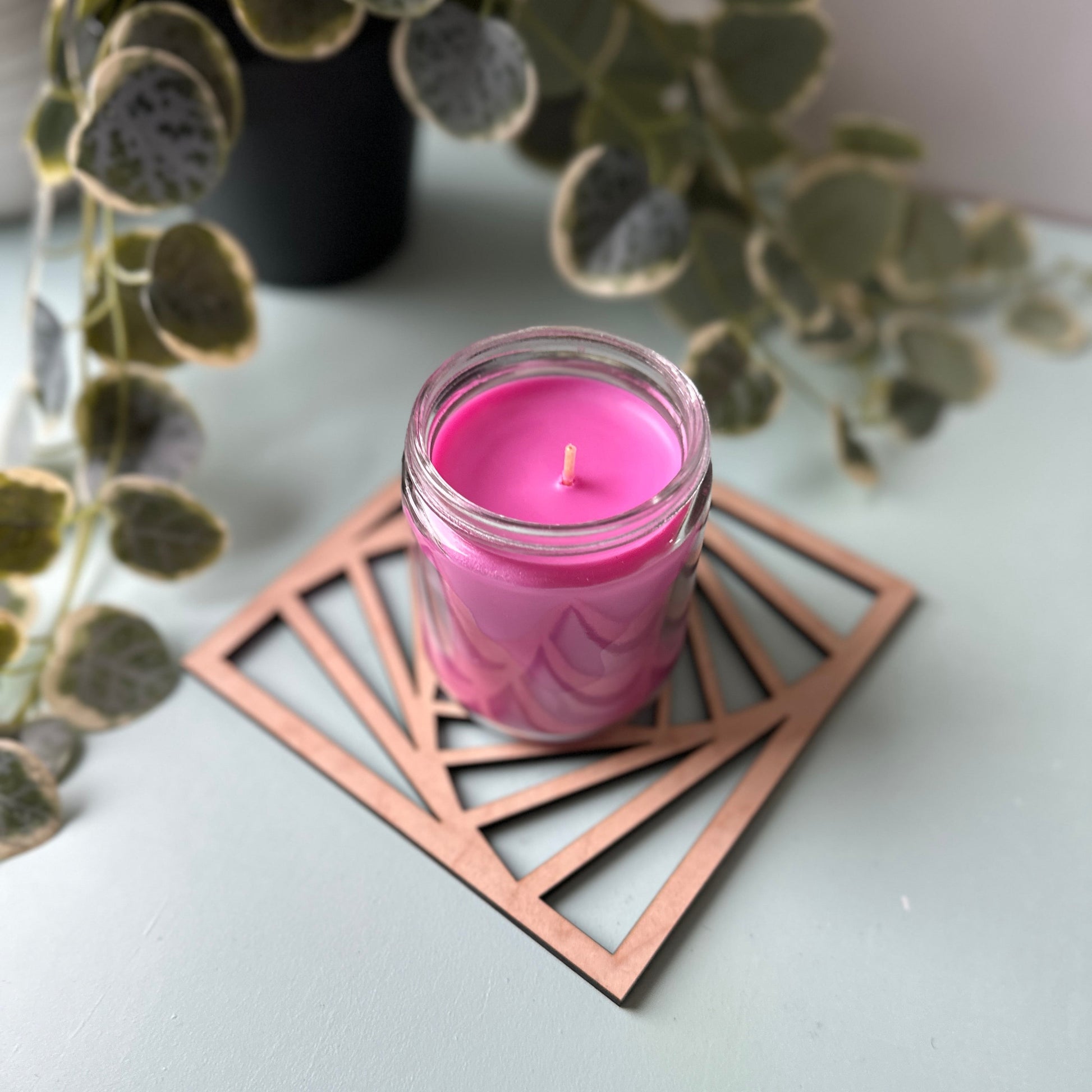 Pink candle in a glass holder on a laser-cut trivet with a decorative design