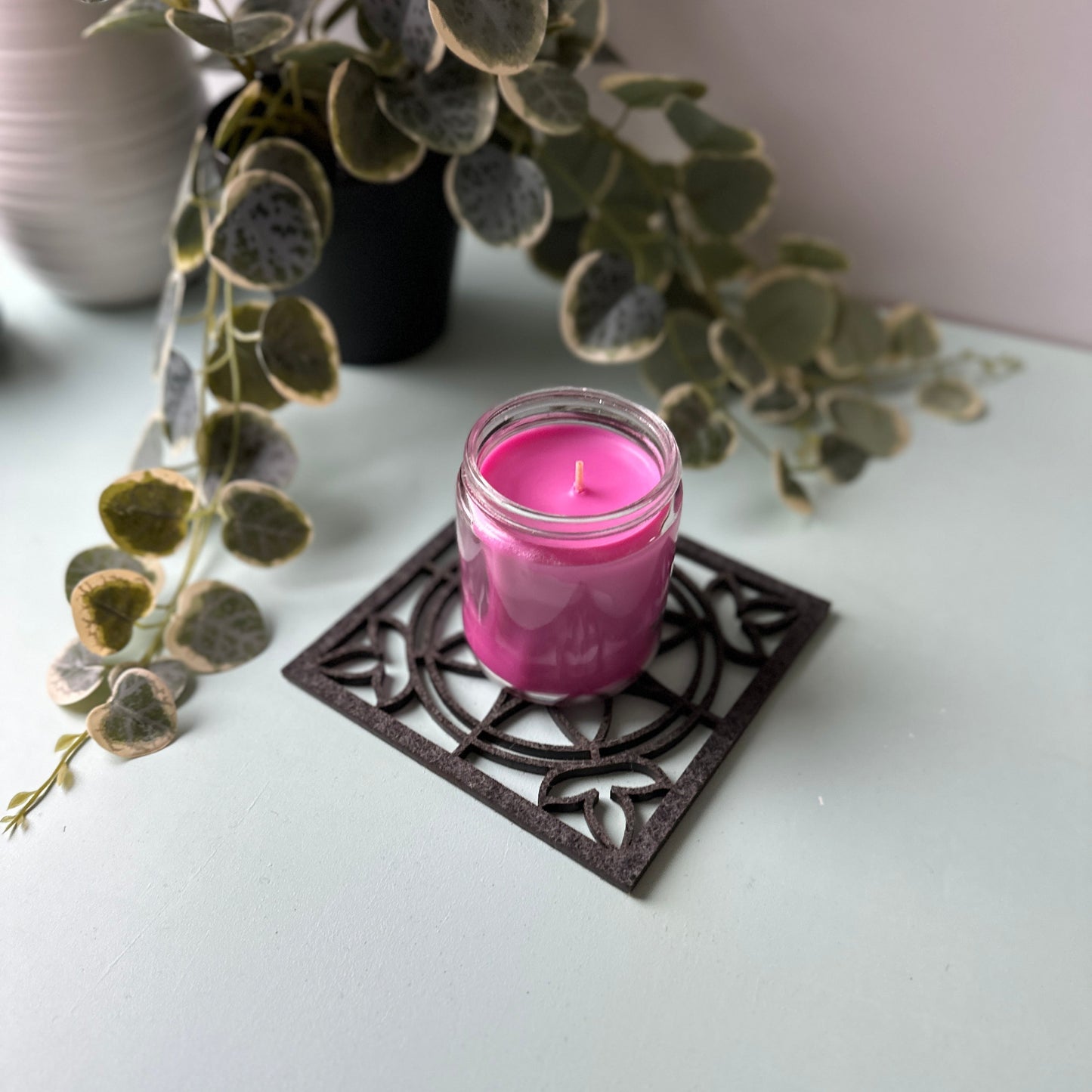 Pink candle in a decorative glass holder on a stained glass trivet with leaves in the background