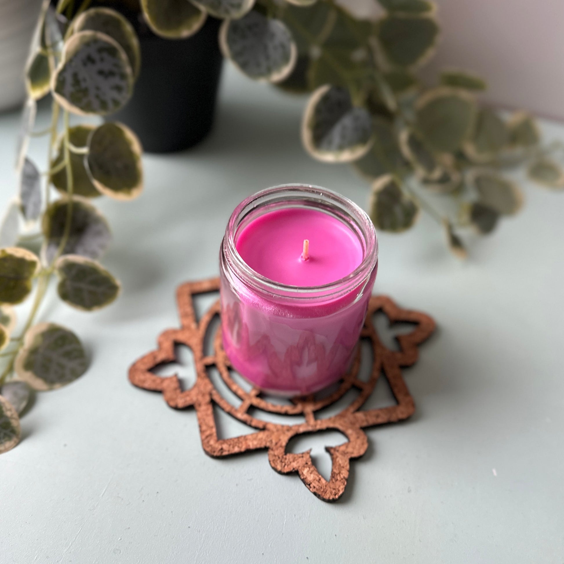 Pink candle in a decorative glass holder on a stained glass trivet with leaves in the background