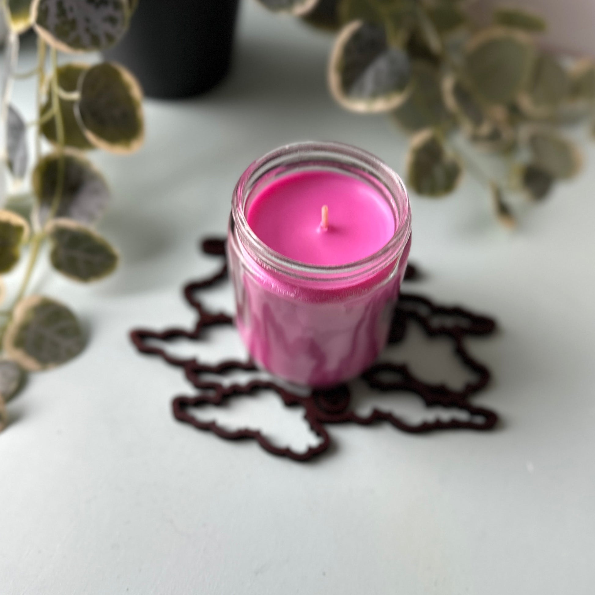 Pink candle in a glass jar on a trivet with green leaves in the background