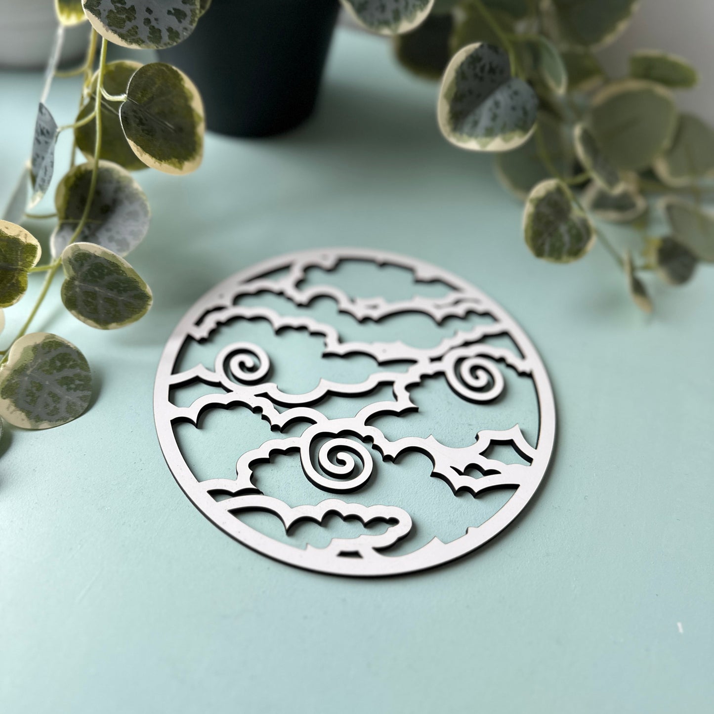 Decorative trivet with intricate patterns on a light blue surface with green leaves in the background