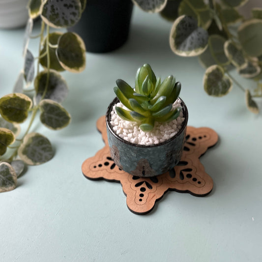Small potted plant on a decorative trivet with a white surface and plants in the background