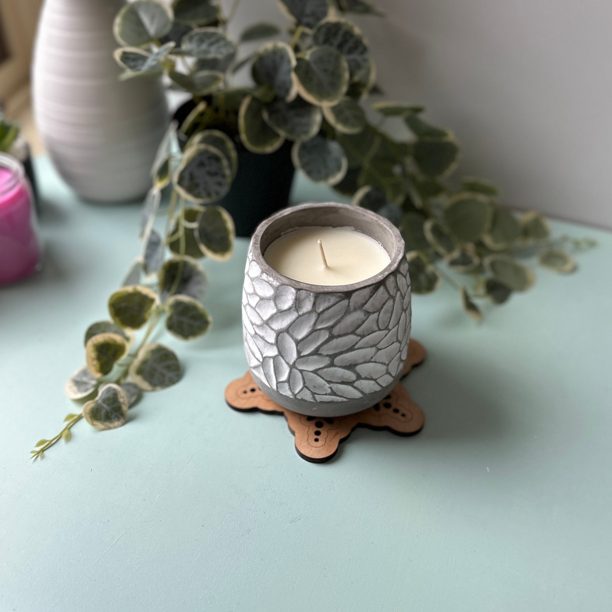 Ceramic candle holder with a lit candle on a trivet with decorative plants.