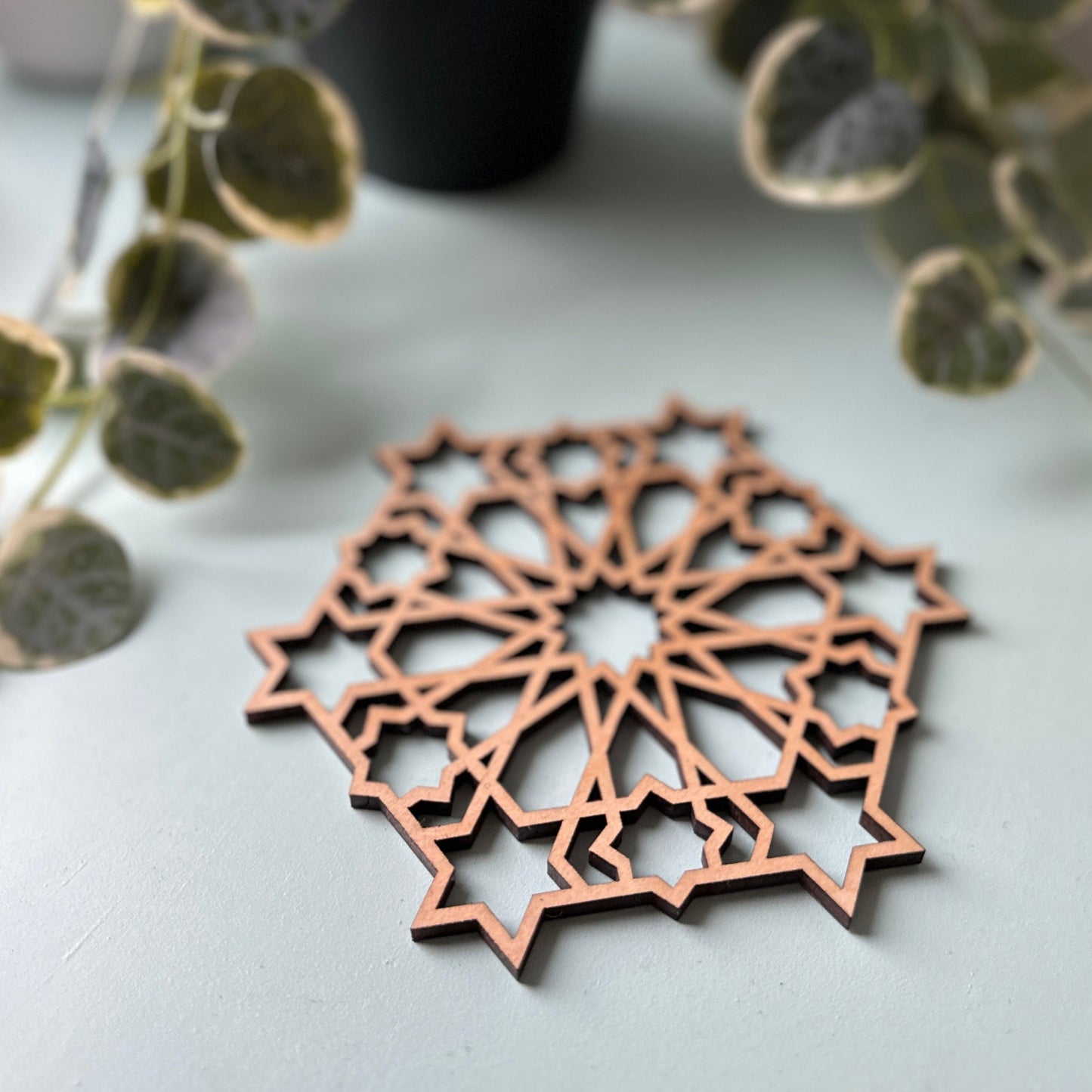 Decorative trivet on a light surface with green foliage in the background
