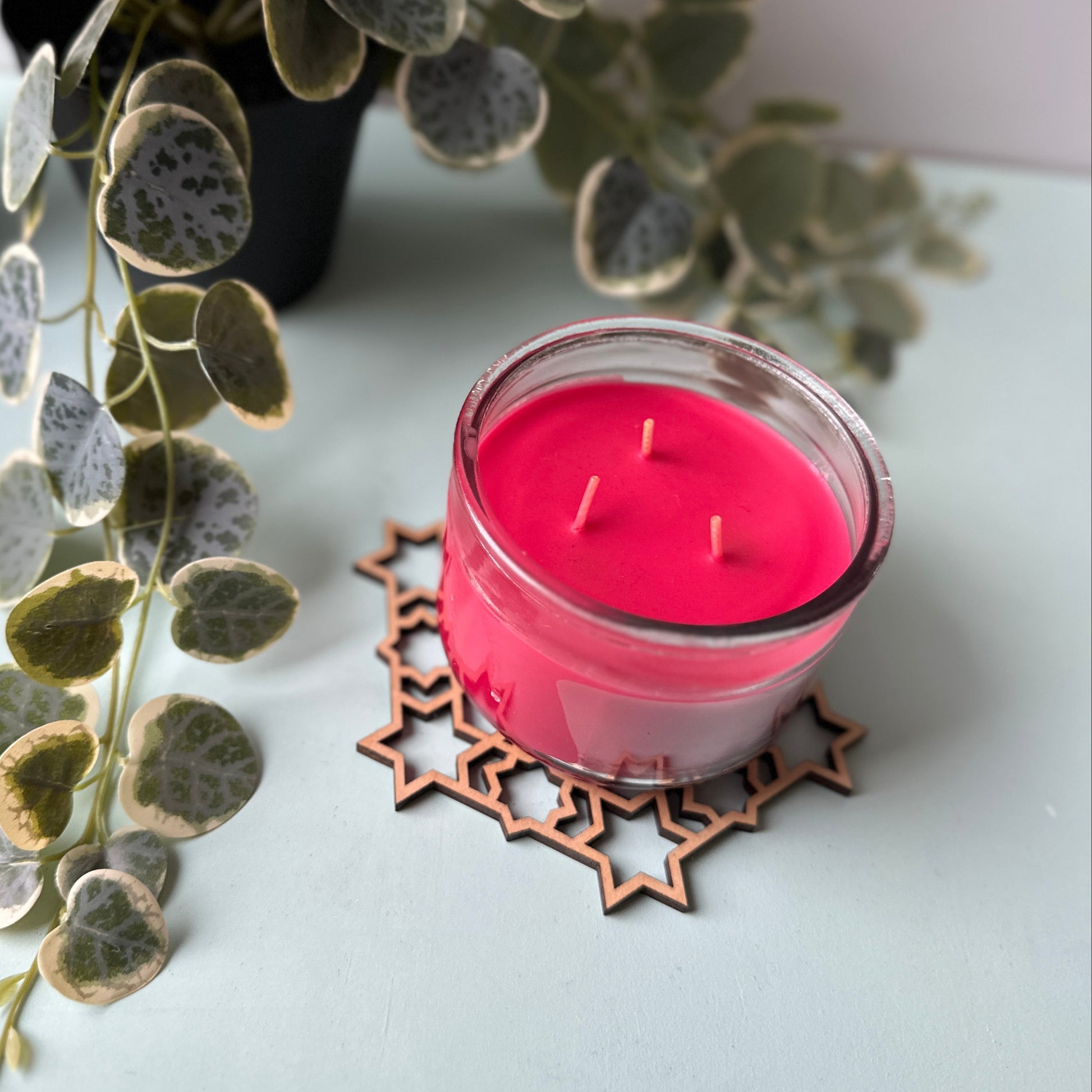 Pink candle in a glass holder on a trivet with green leaves in the background