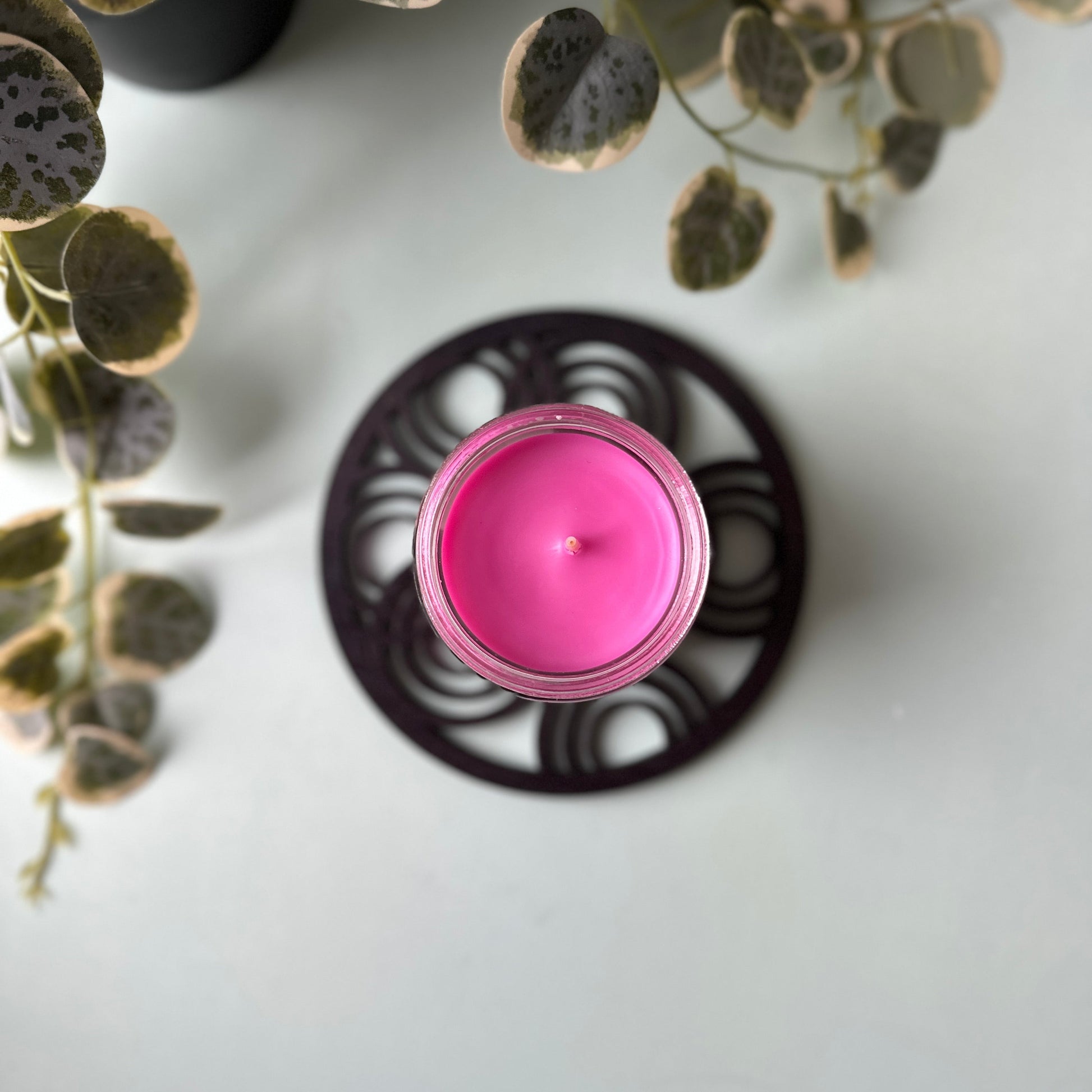 Pink candle in a decorative holder with green leaves on a white surface