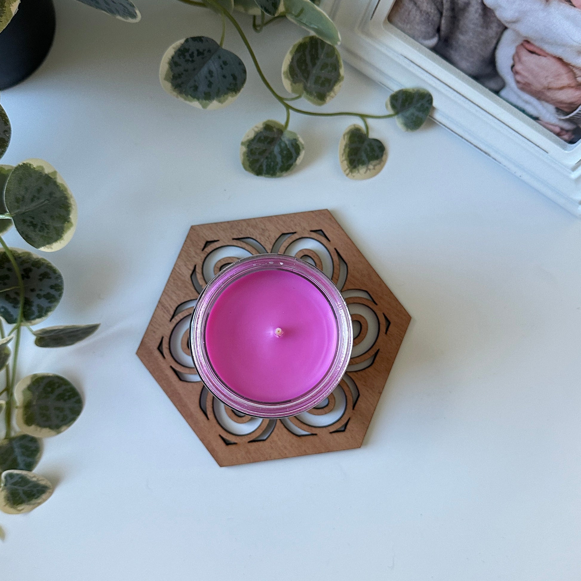 Pink candle in a decorative holder on a white surface with a framed photo and plant.