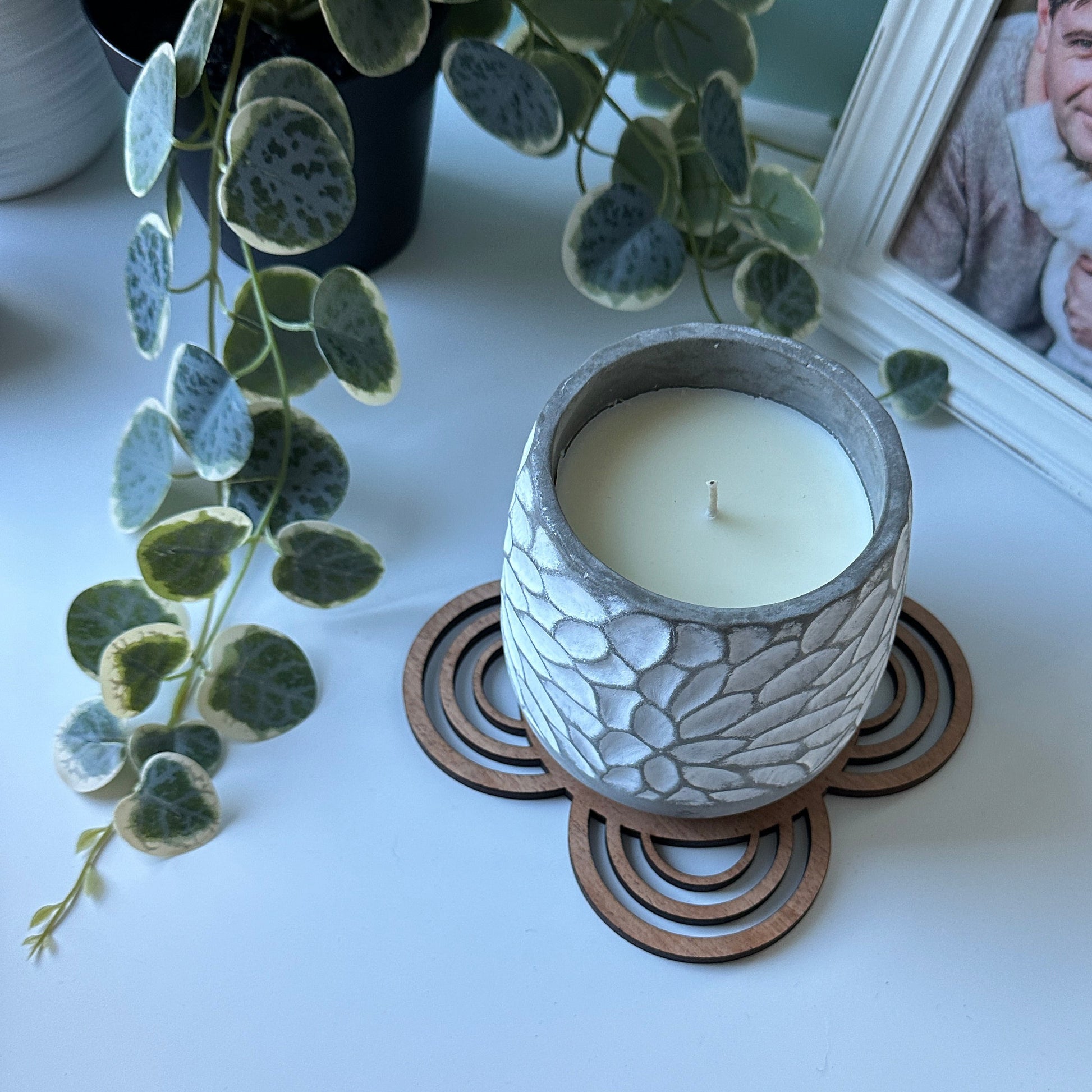 Candle in a textured holder on a trivet with a framed photo of two children in the background.