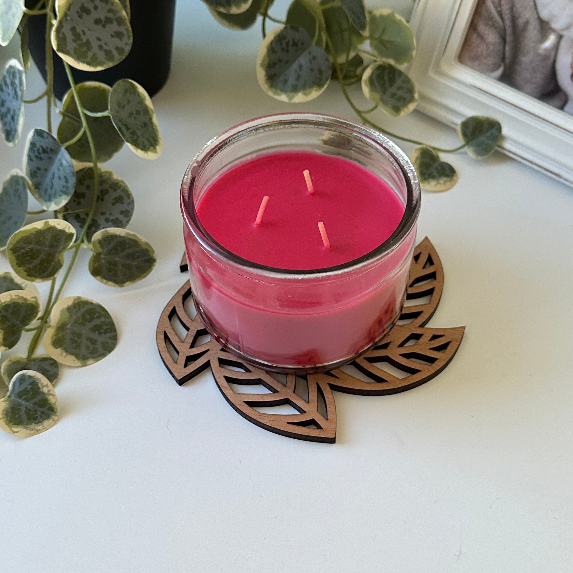 Pink candle in a decorative holder with leaves and a photo frame in the background