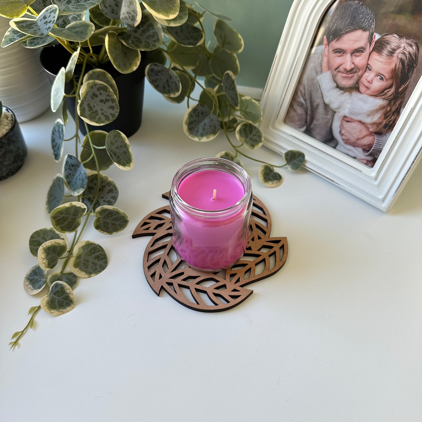 White candle on a decorative trivet with leaves and a photo frame in the background