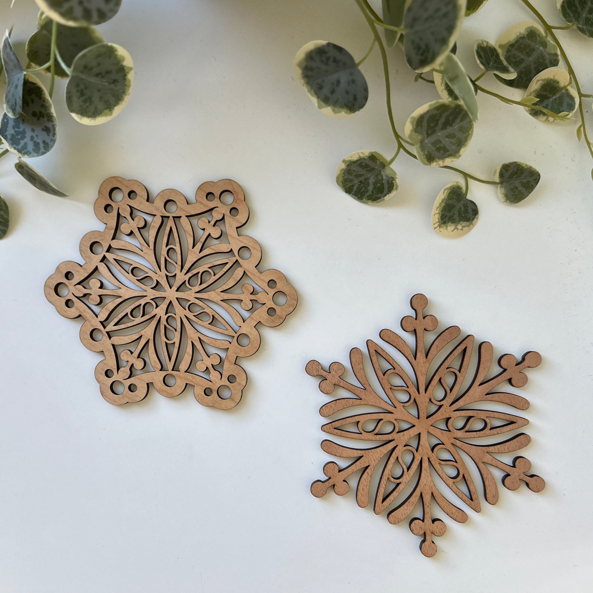 Two wooden snowflake trivets on a white surface with green leaves.
