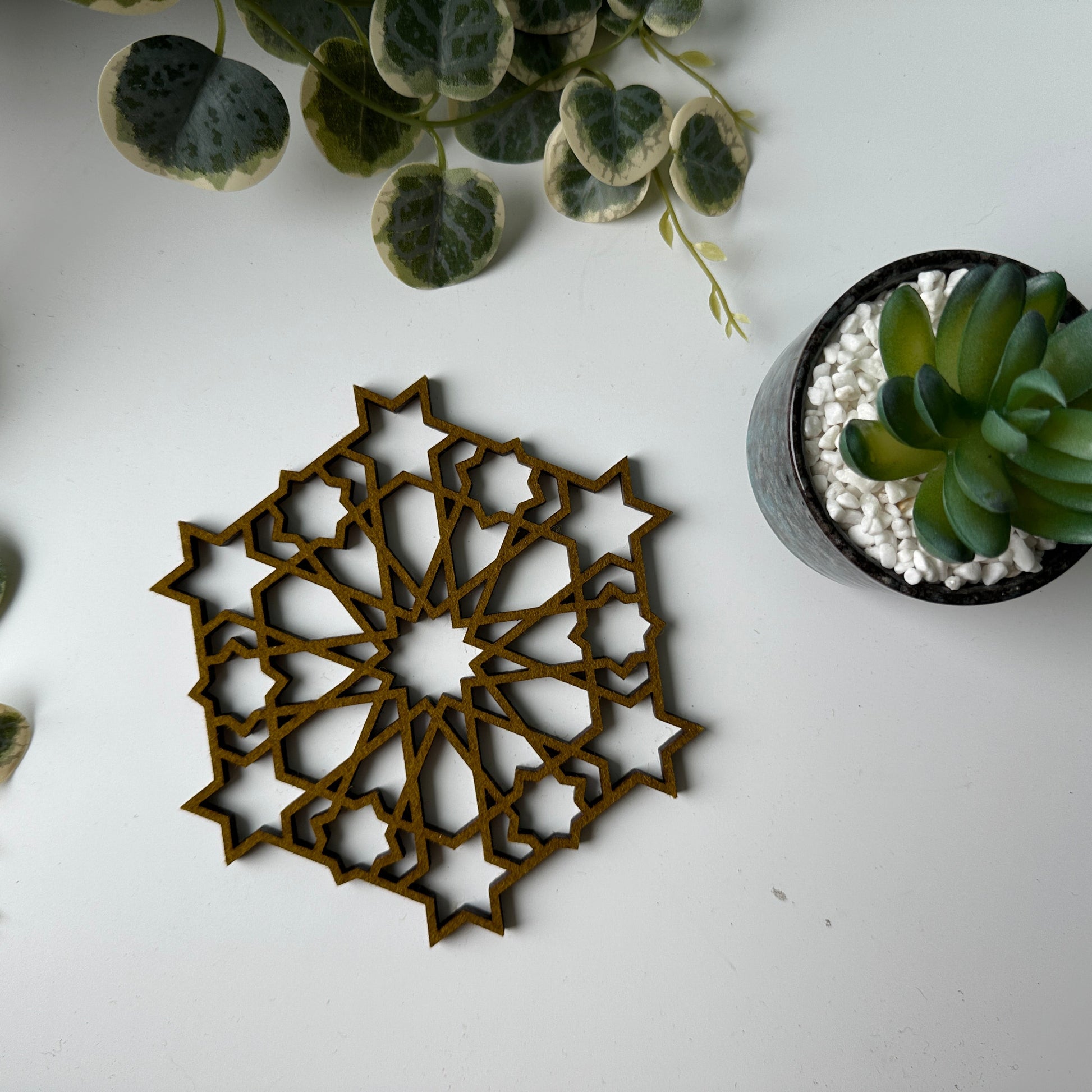Decorative trivet with geometric pattern on a white surface with plants.