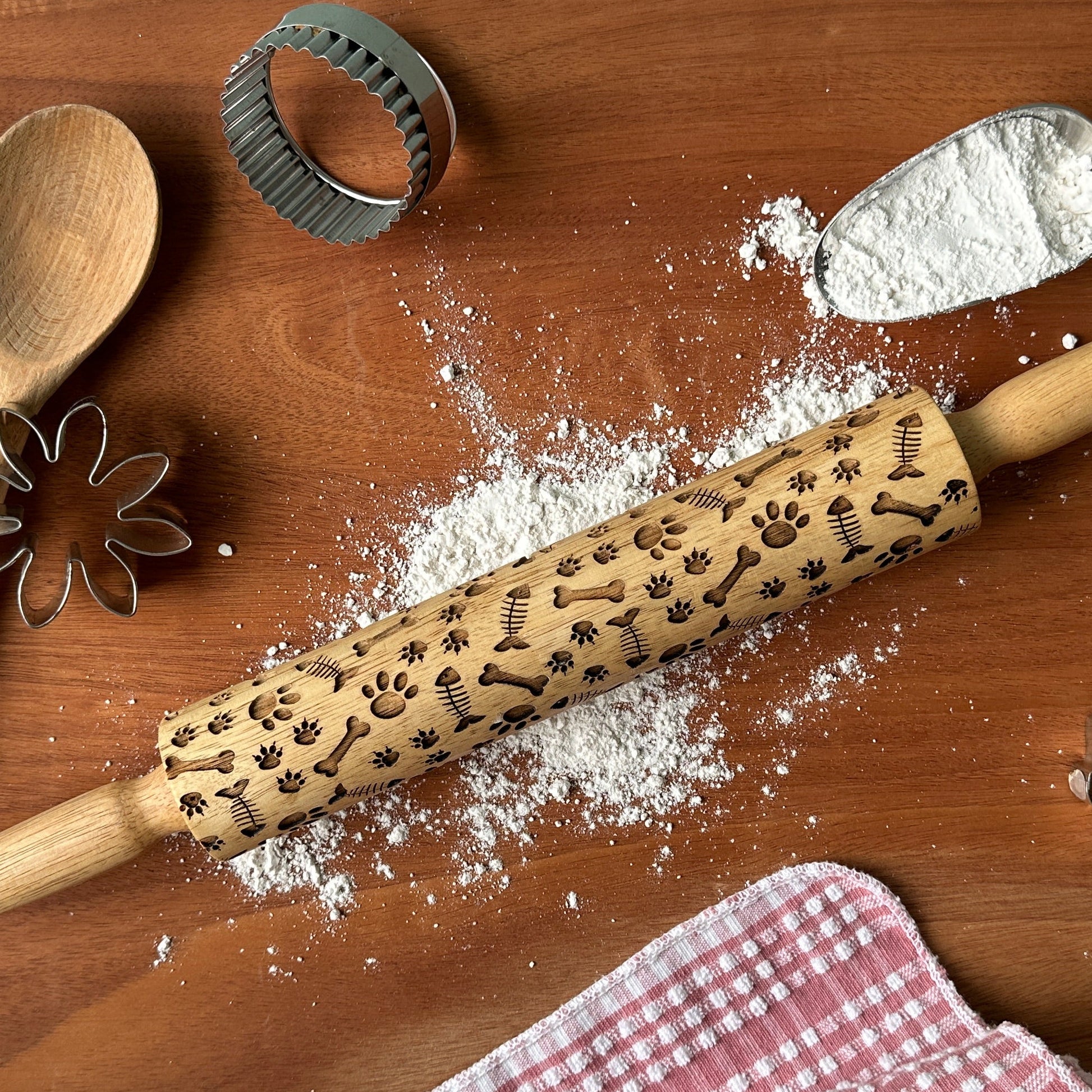 Baking tools including a rolling pin, spatula, and measuring cups on a wooden surface with flour.