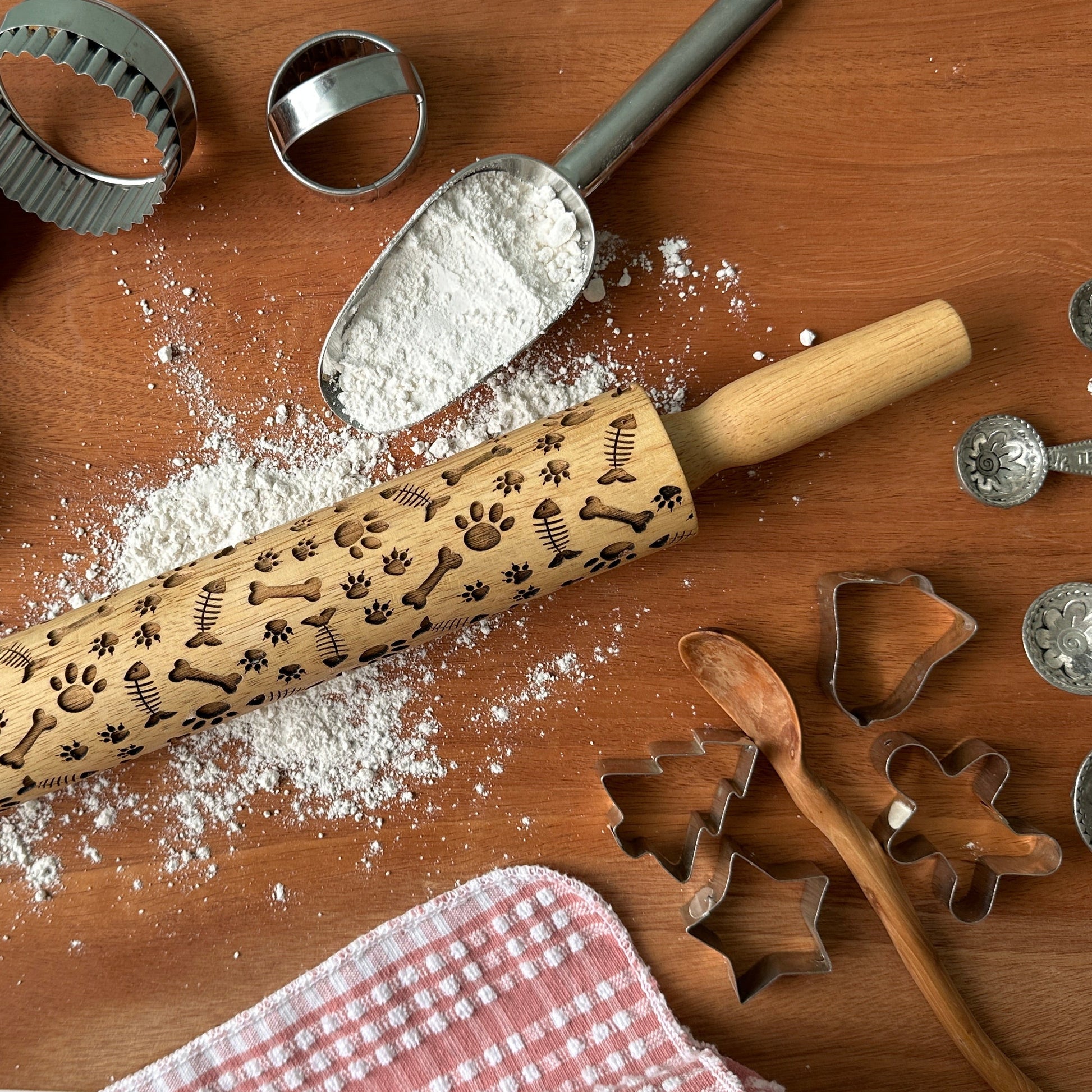 Baking tools including a rolling pin, cookie cutters, and flour on a wooden surface.