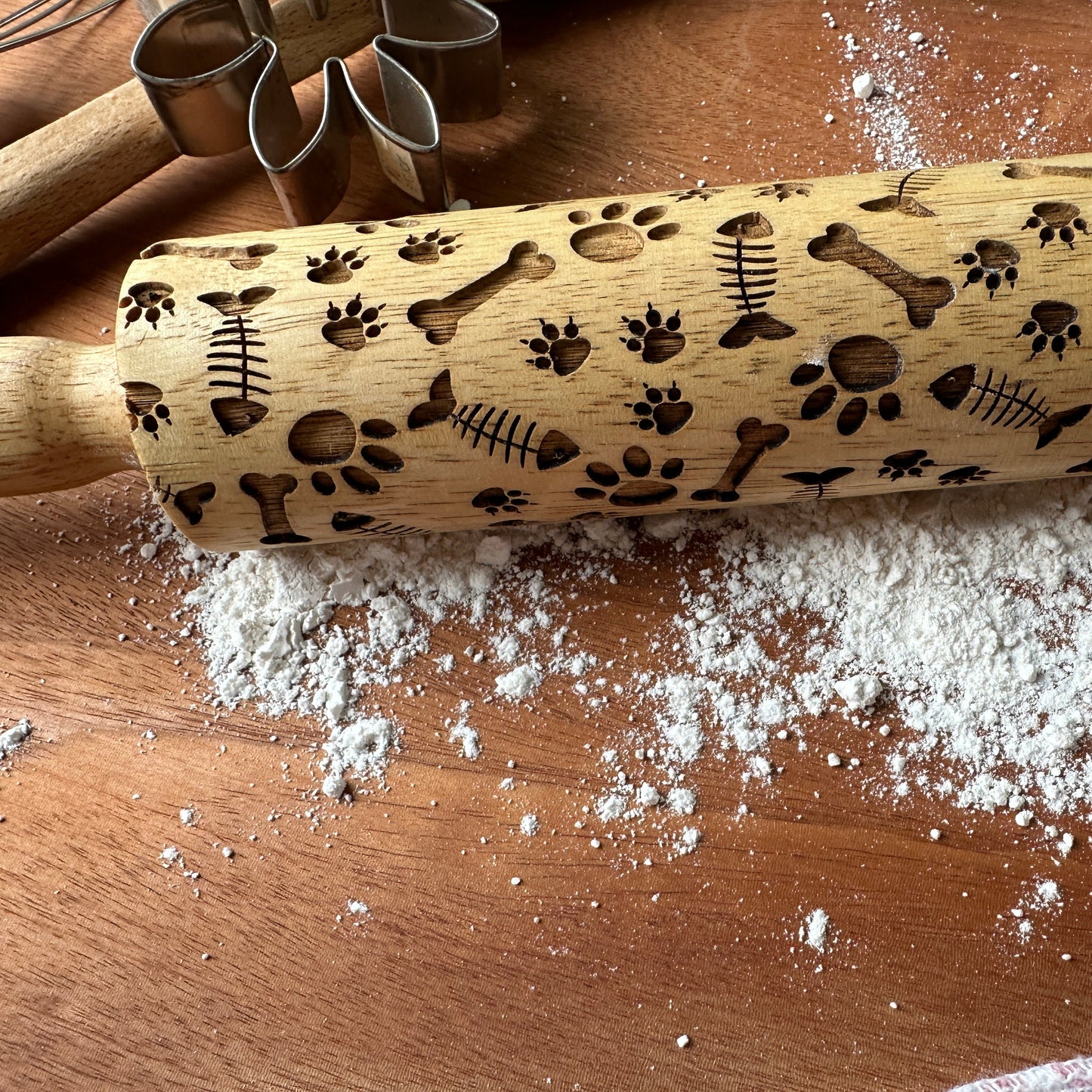 Wooden rolling pin with embossed designs on a wooden surface with flour.