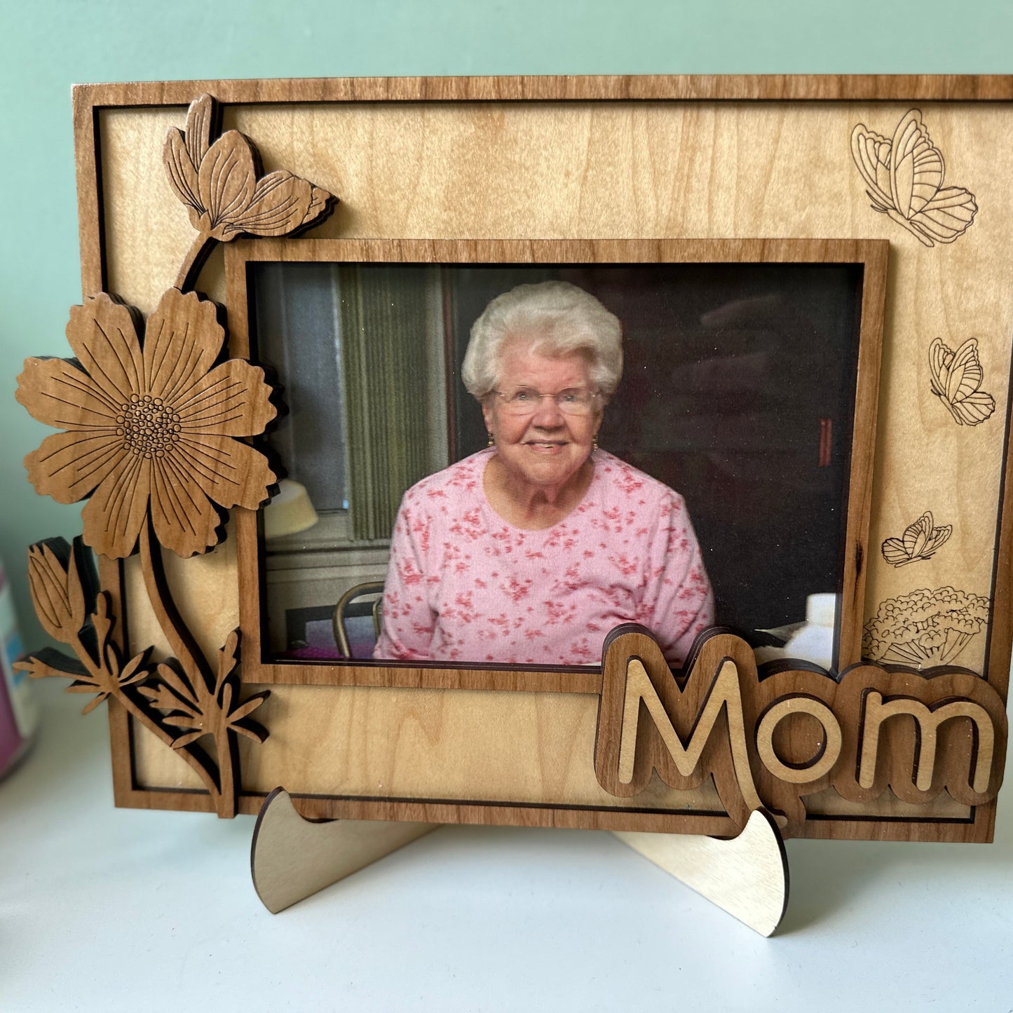 Wooden photo frame with floral designs and 'Mom' engraving, featuring a photo of an elderly woman.