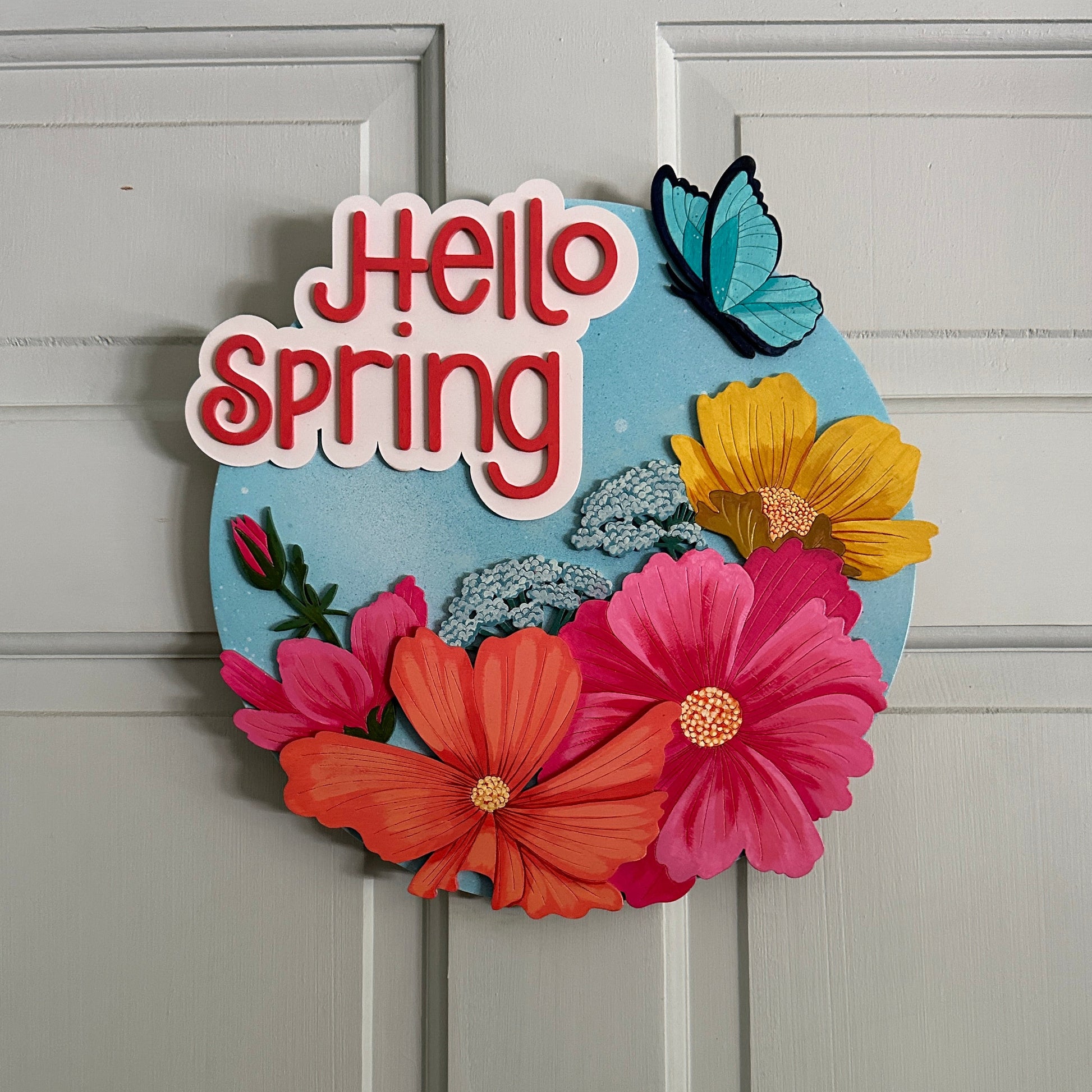 Decorative wreath with colorful flowers and 'Hello Spring' text on a gray door.