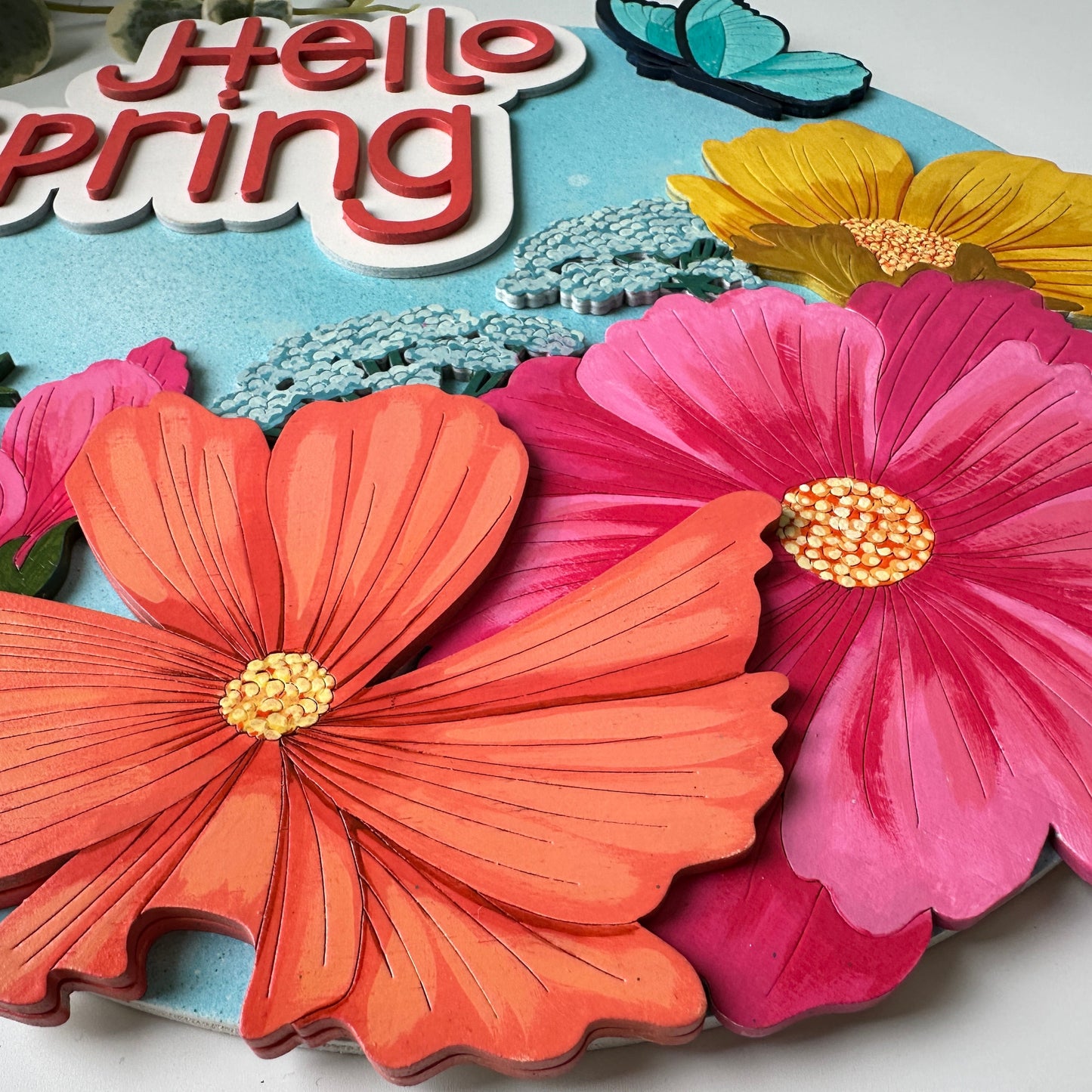Colorful paper flowers with 'Hello Spring' text on a blue background