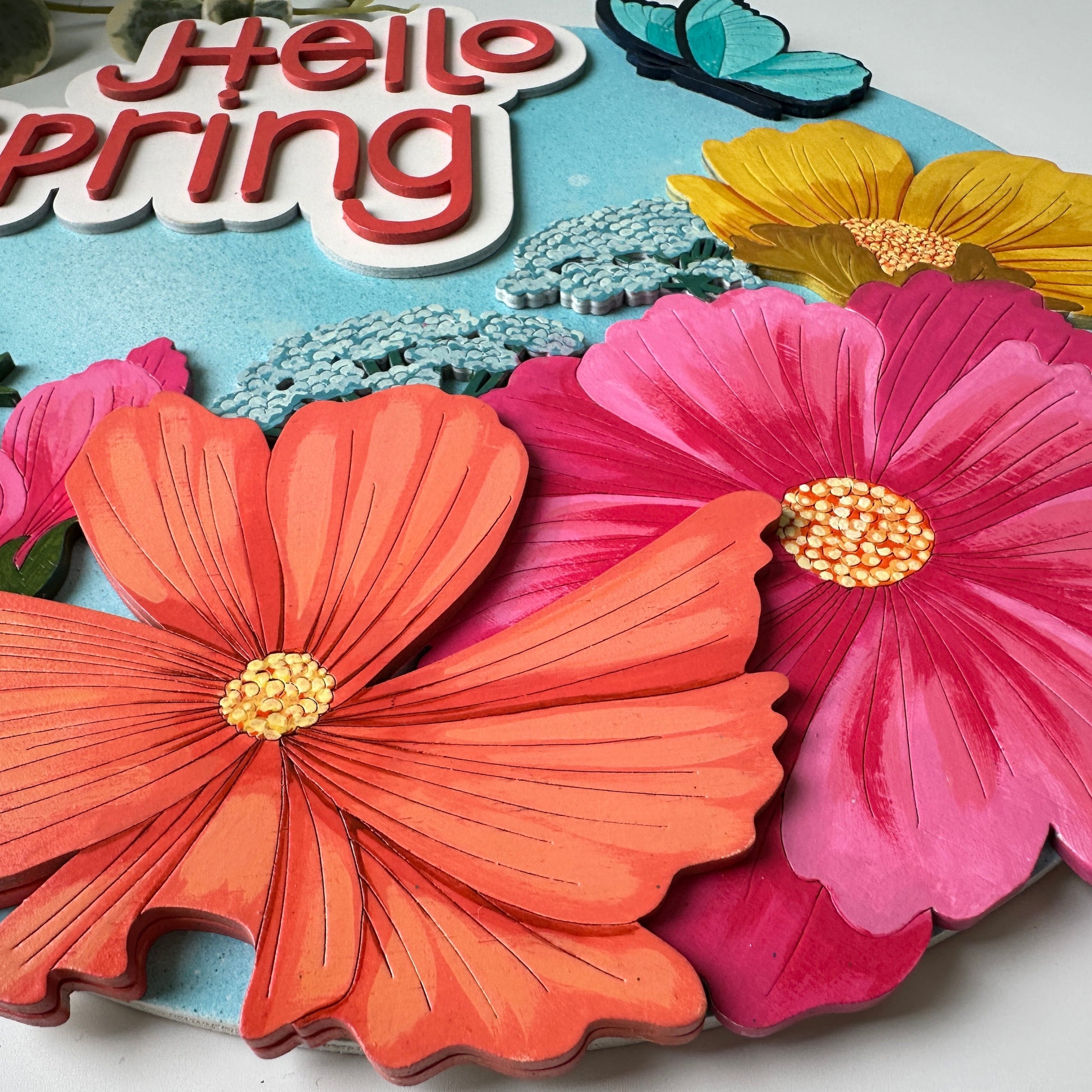 Colorful paper flowers with 'Hello Spring' text on a blue background