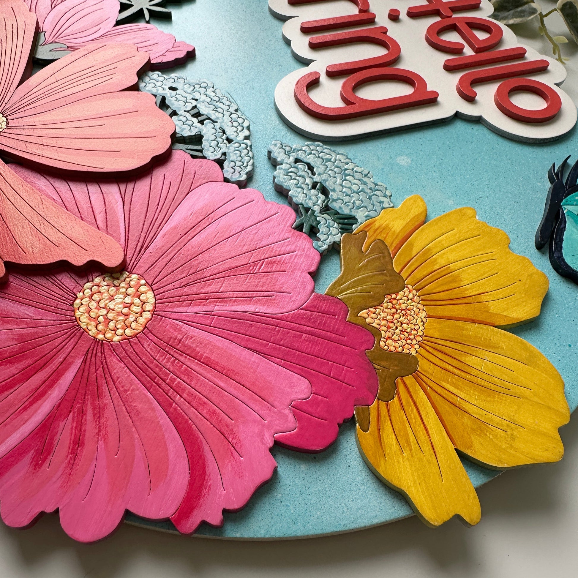 Decorative wall art with flowers and 'Hello Spring' text on a blue background