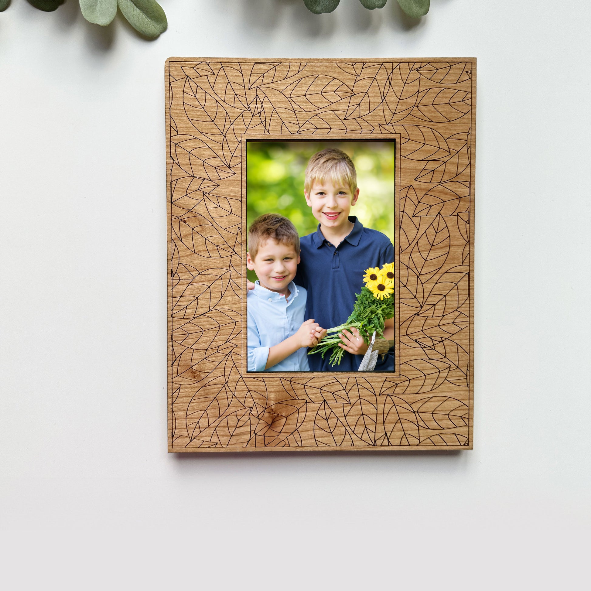 Wooden photo frame with leaf pattern holding a photo of two children with flowers on a white background.