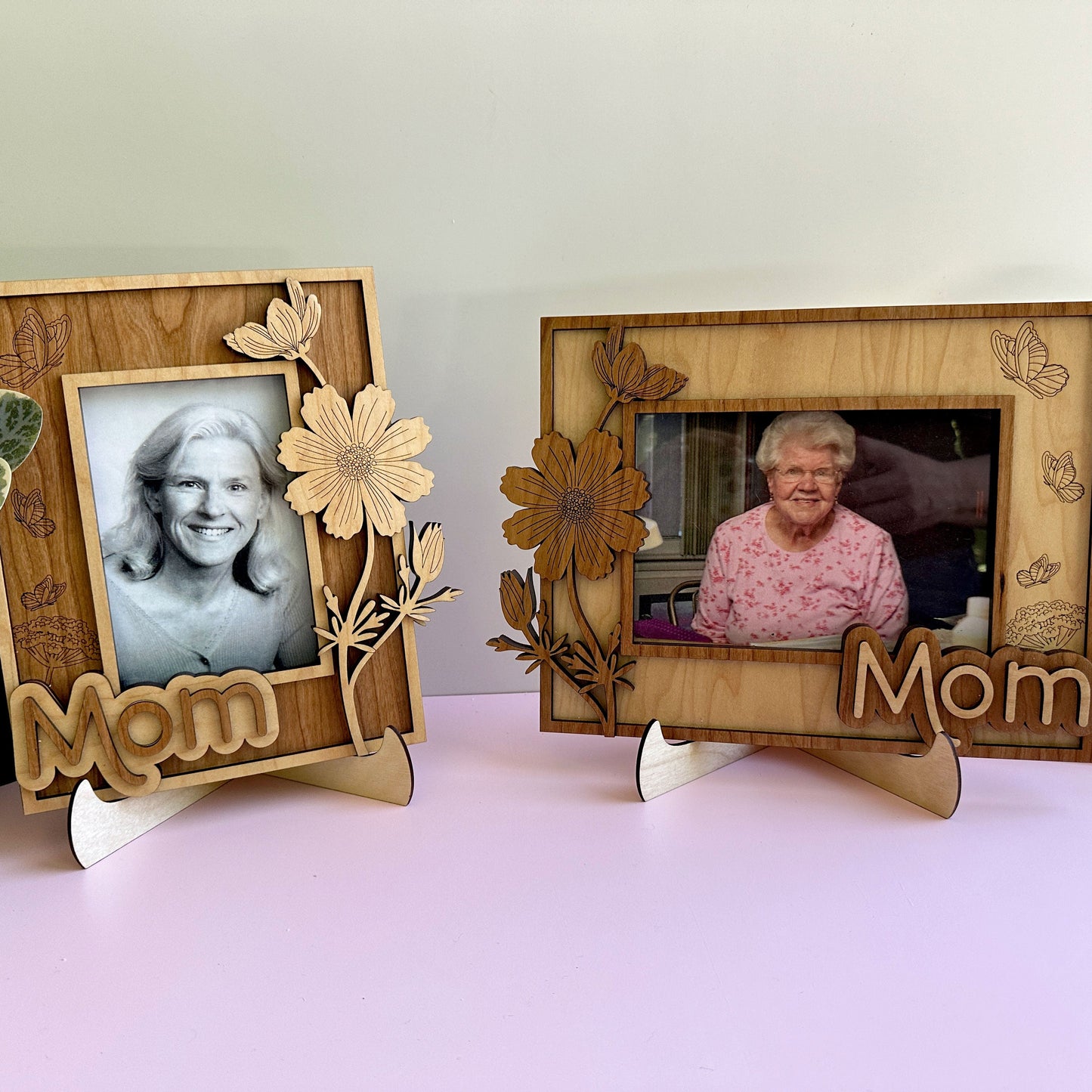 Two wooden photo frames with floral designs and 'Mom' text on a light pink surface.